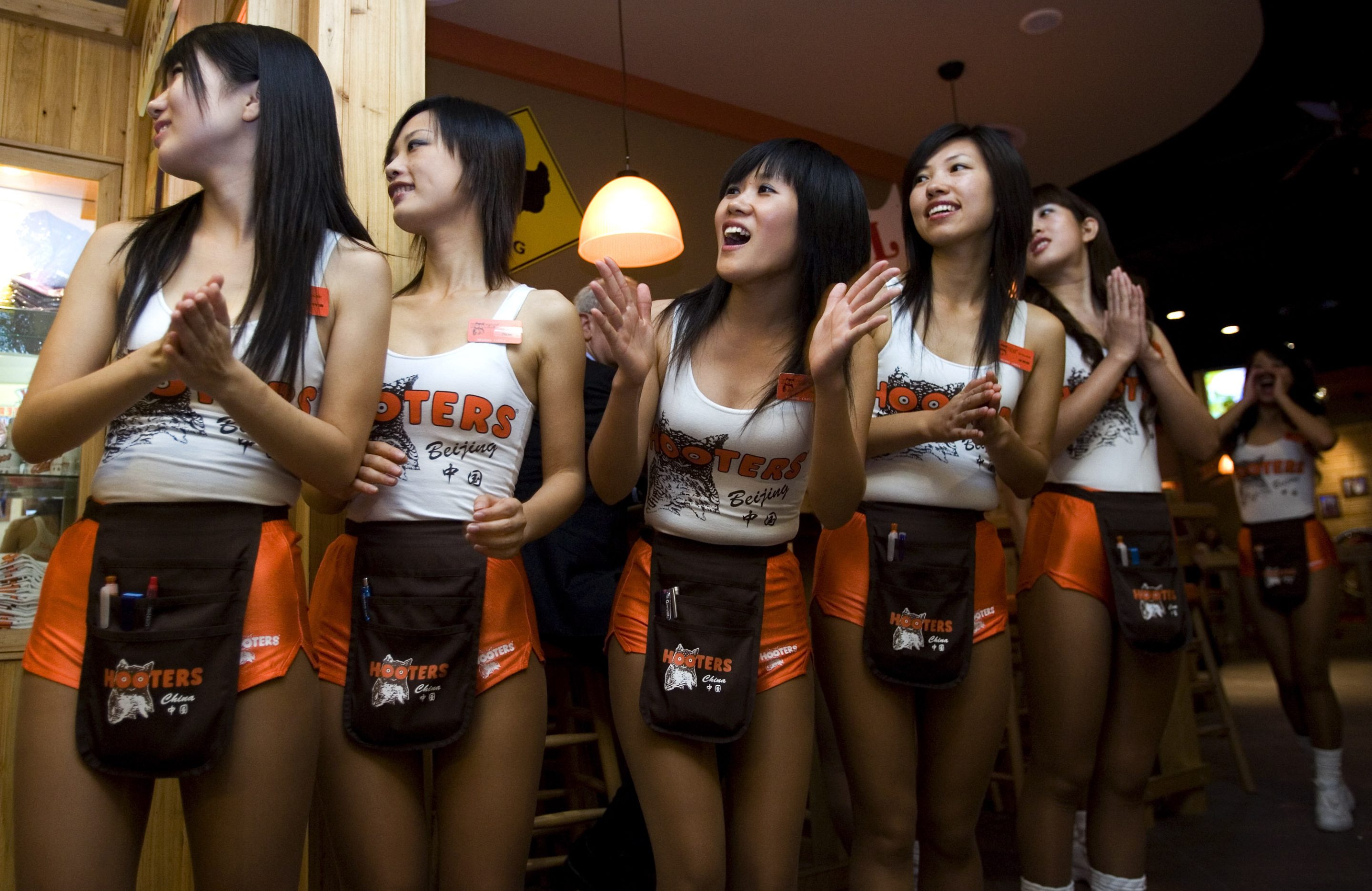 Chinese waitresses dressed in orange shorts and t-shirts cheers while welcoming the arriving guests at the Hooters restaurant in Beijing, China, Sept. 10, 2007. 