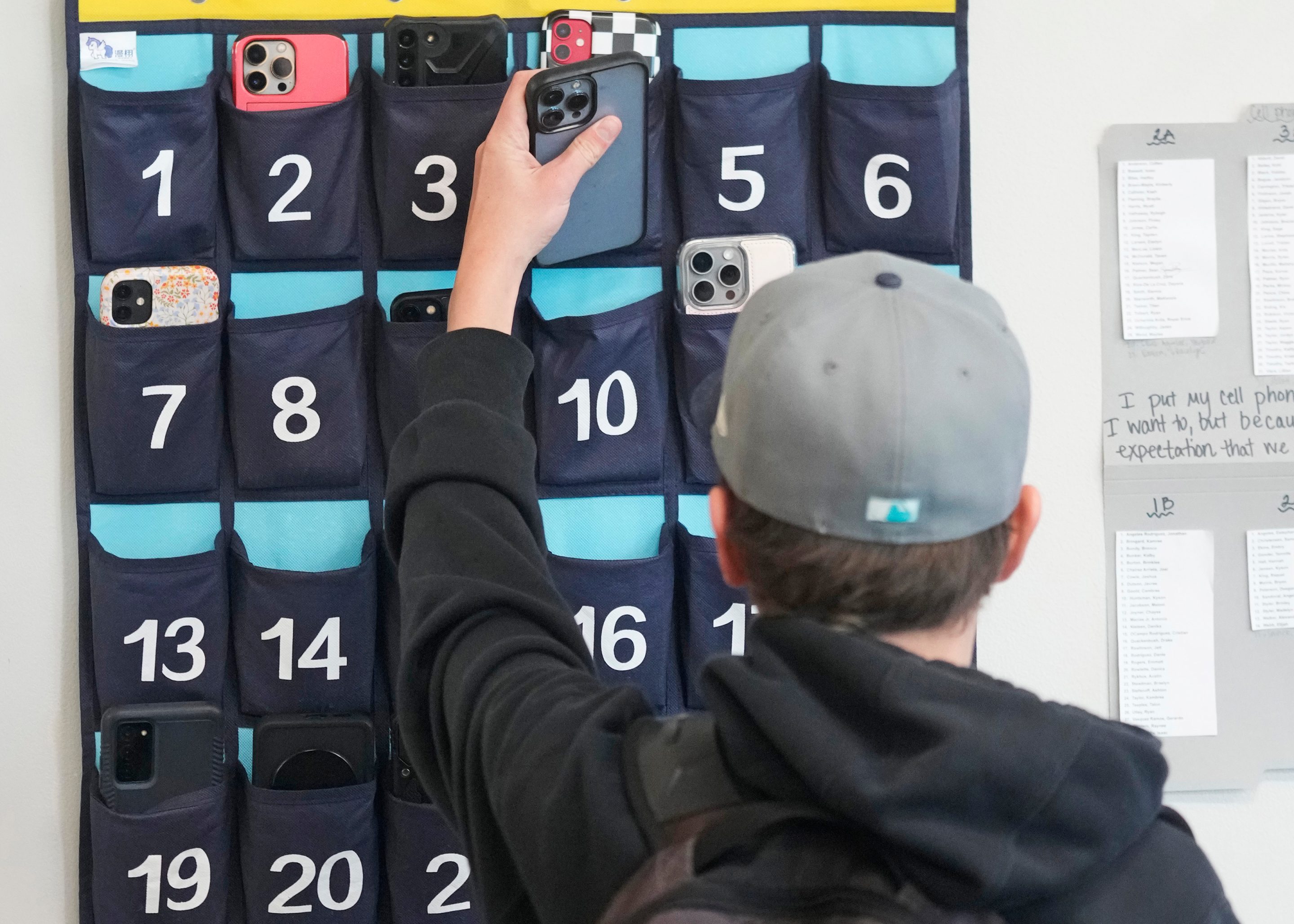 A ninth grader places his cellphone into a phone holder as he enters class at Delta High School, on Feb. 23, 2024, in Delta, Utah.
