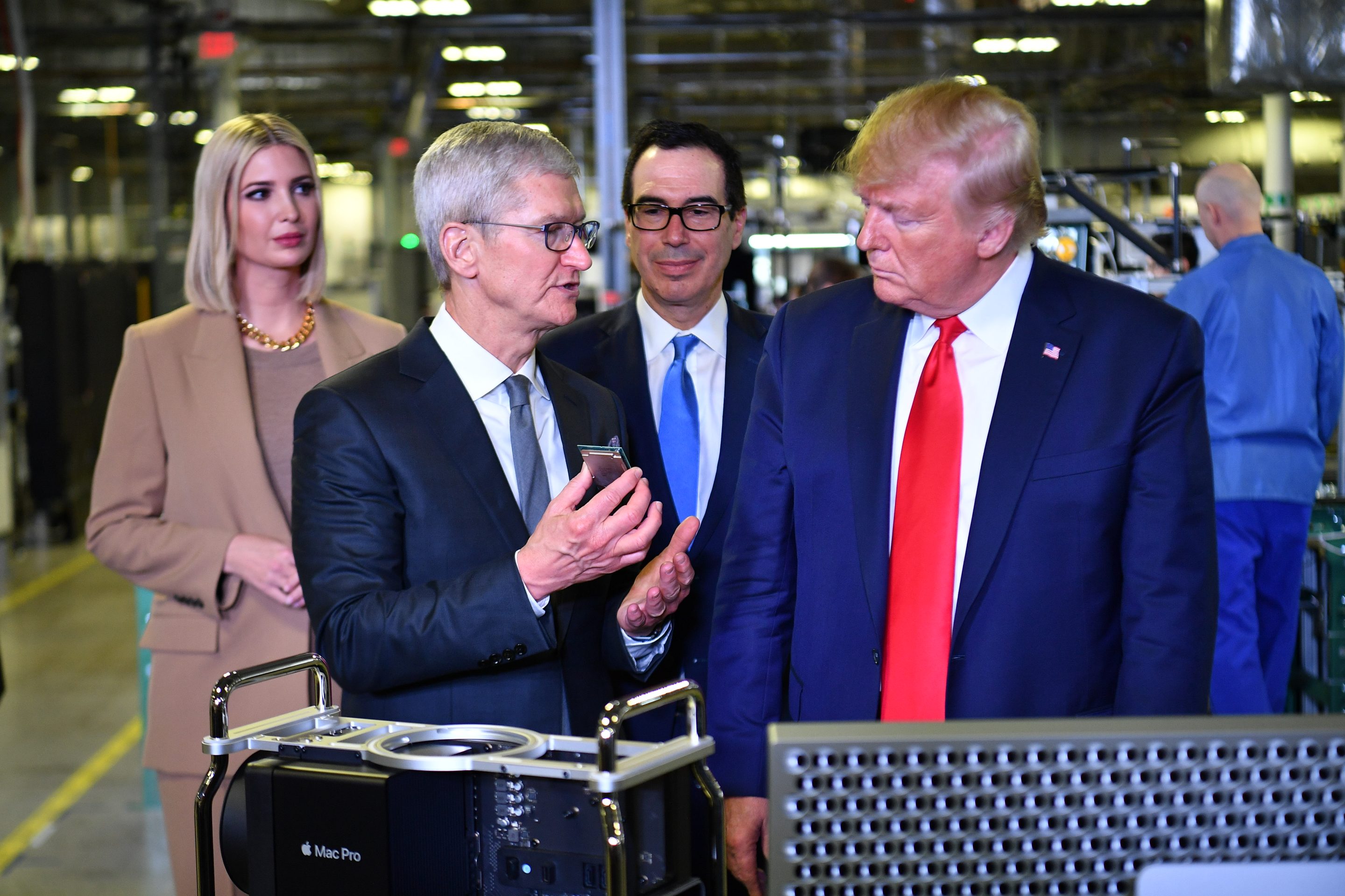 Tim Cook shows Donald Trump a piece of technology while standing in a factory.