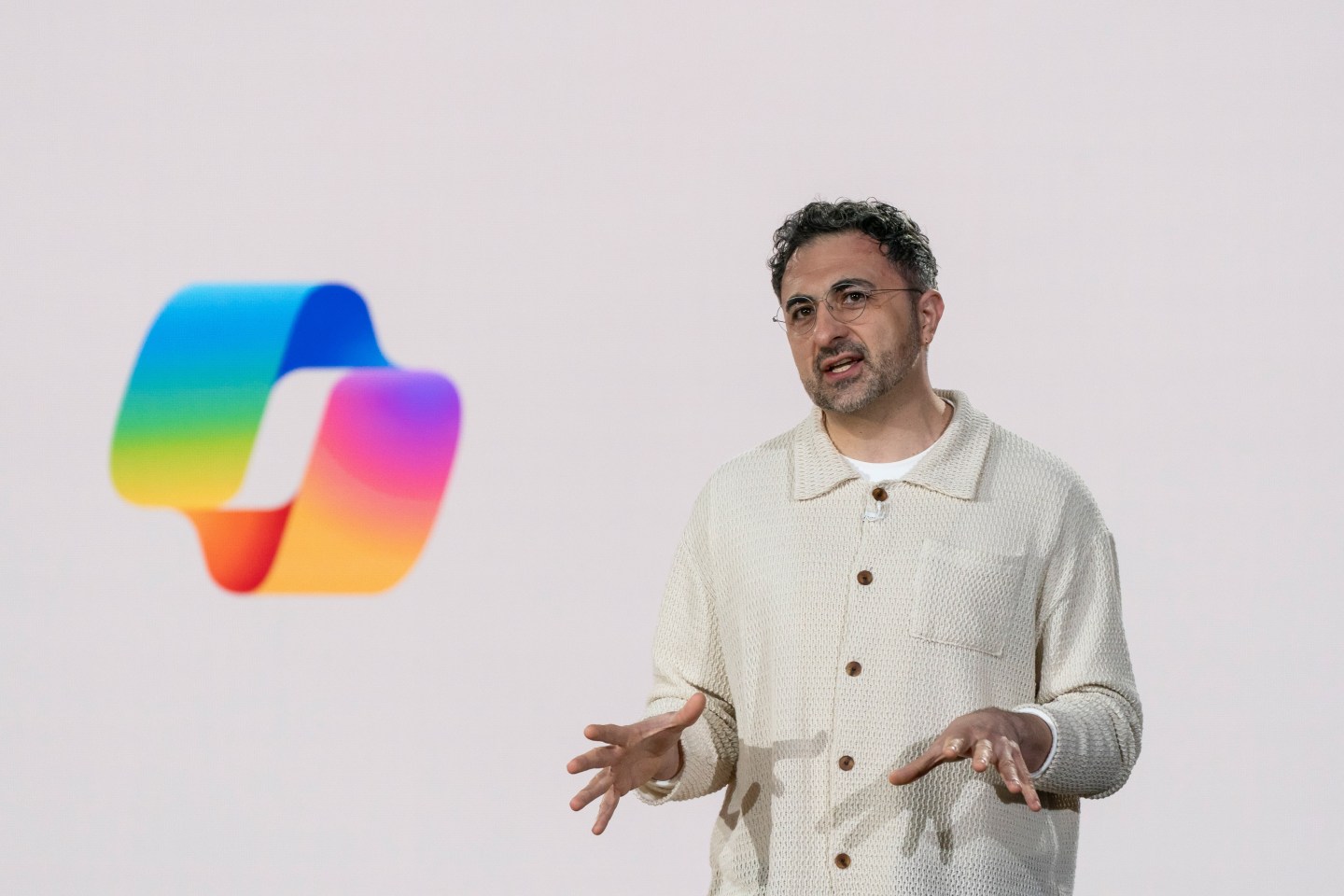 Mustafa Suleyman in a white shirt with the copilot logo behind him.