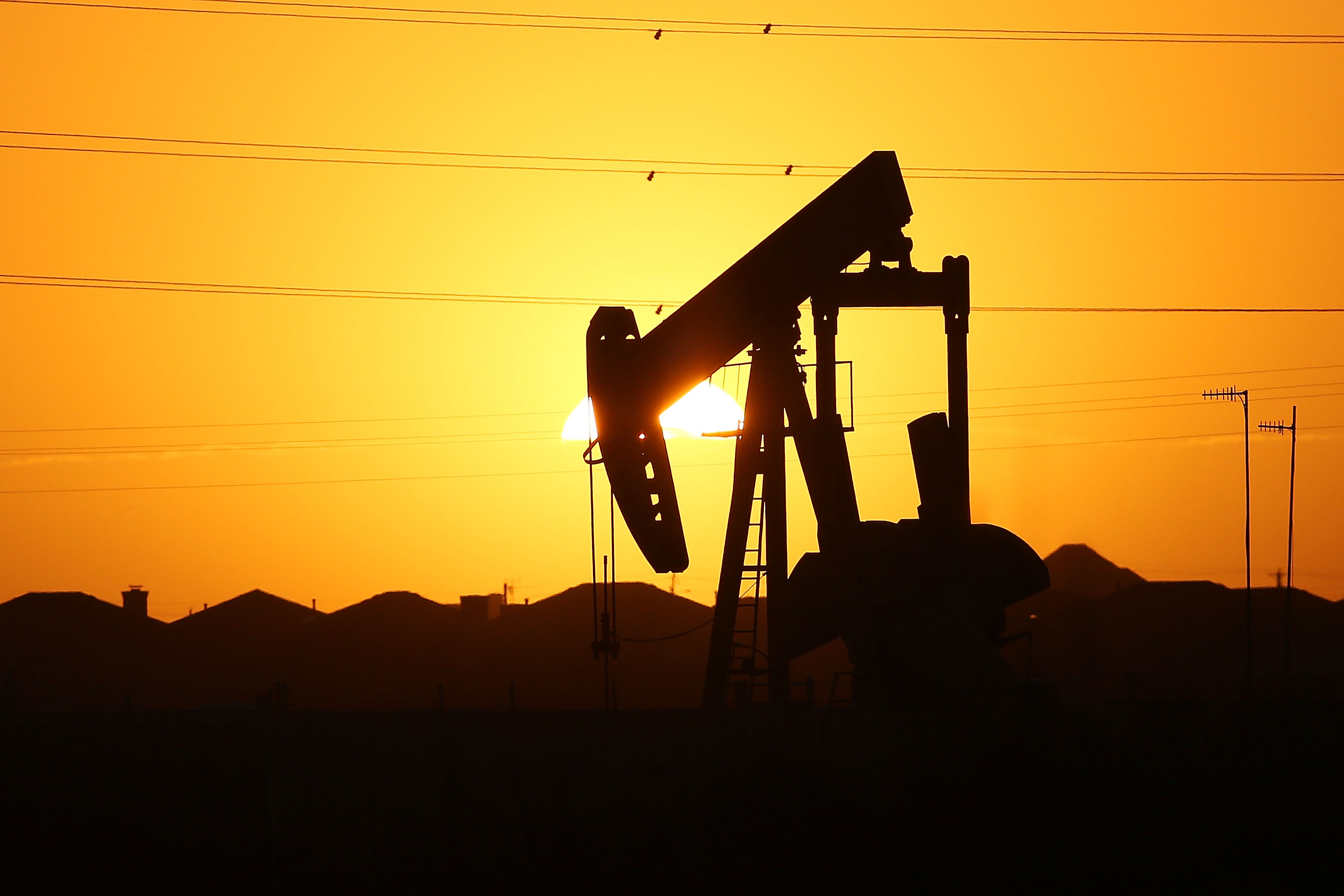 An oil pumpjack partially obscures the setting sun.