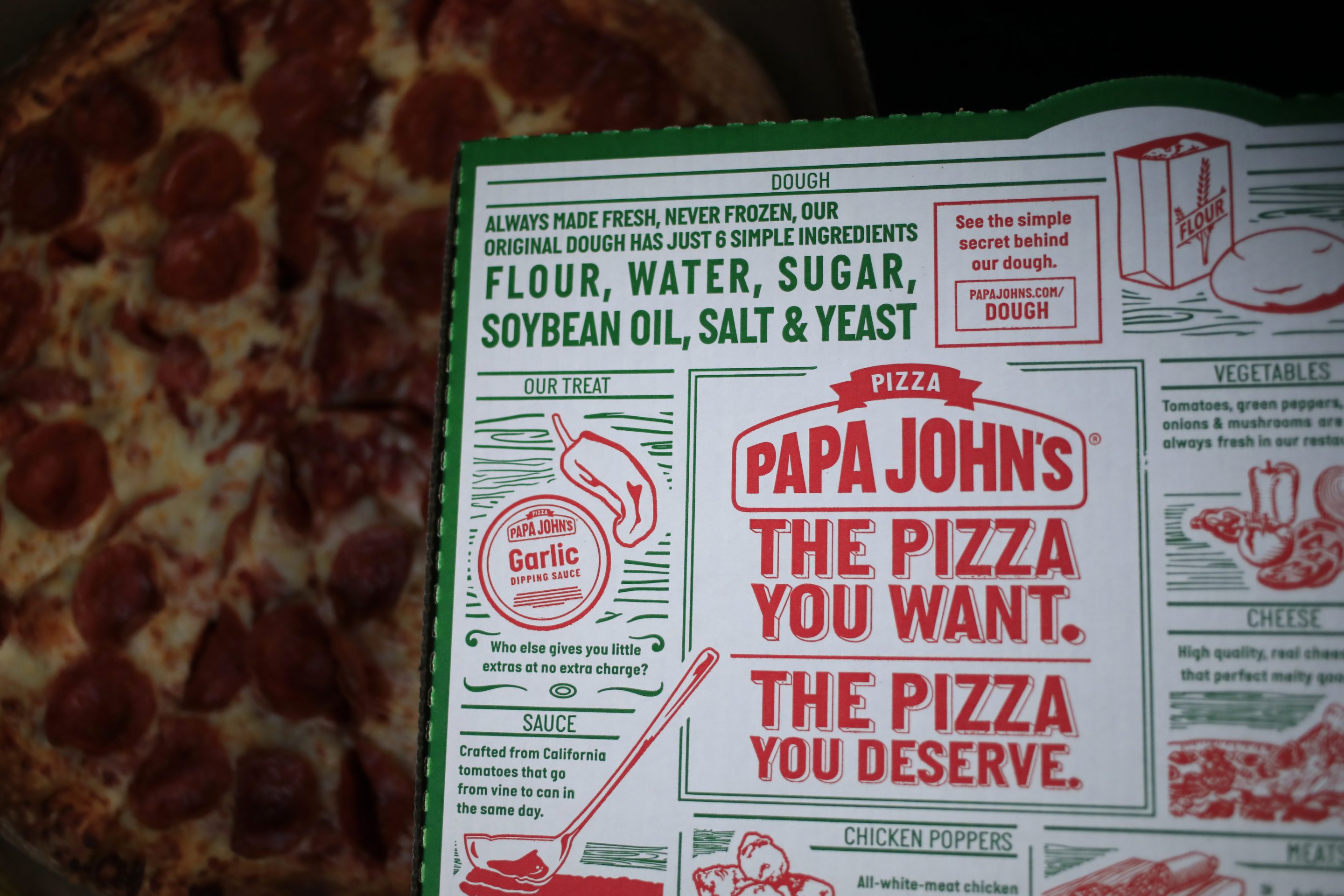 A pizza box in front of a cheese and pepperoni pizza.