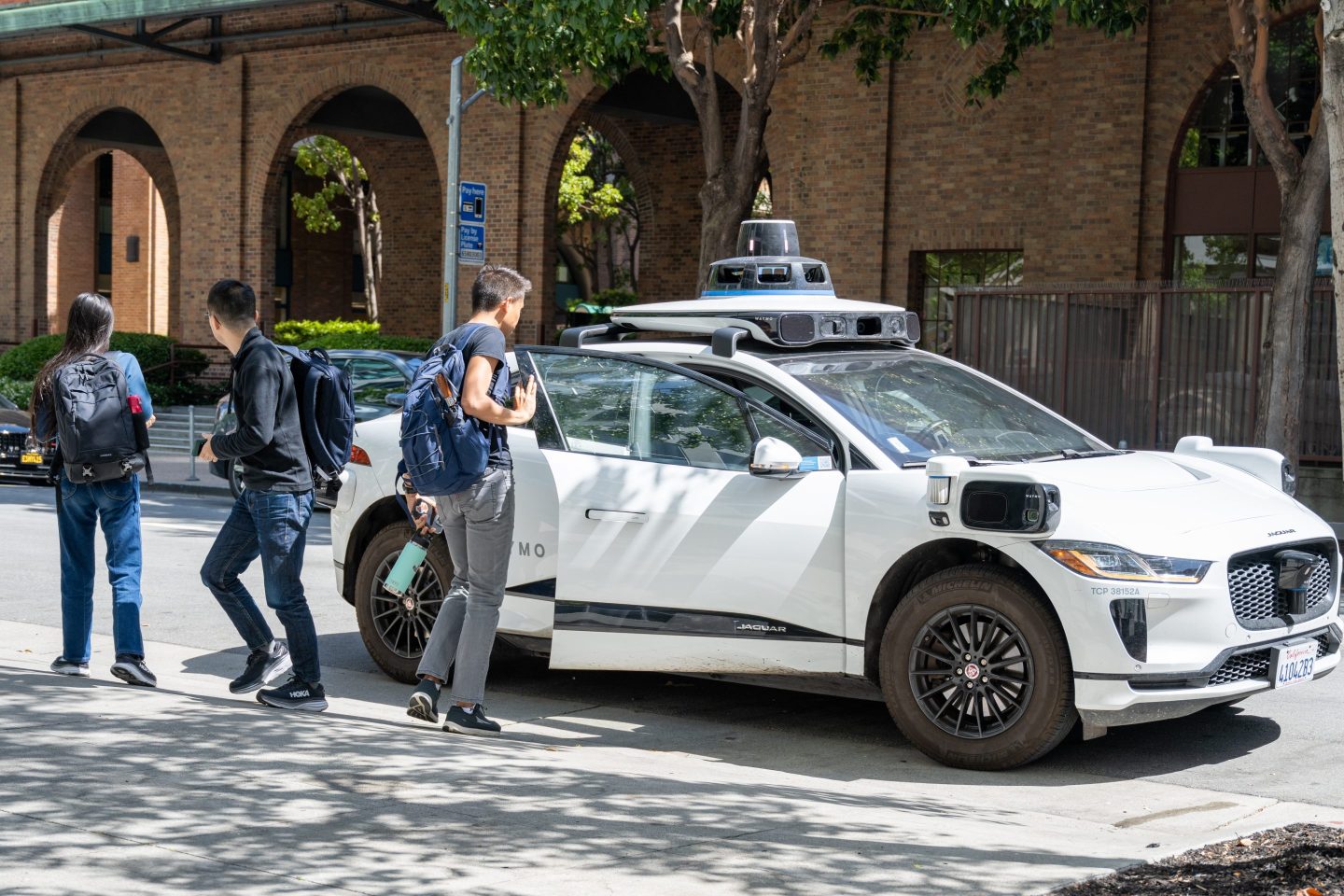 Students exit a Waymo car stopped on the street.