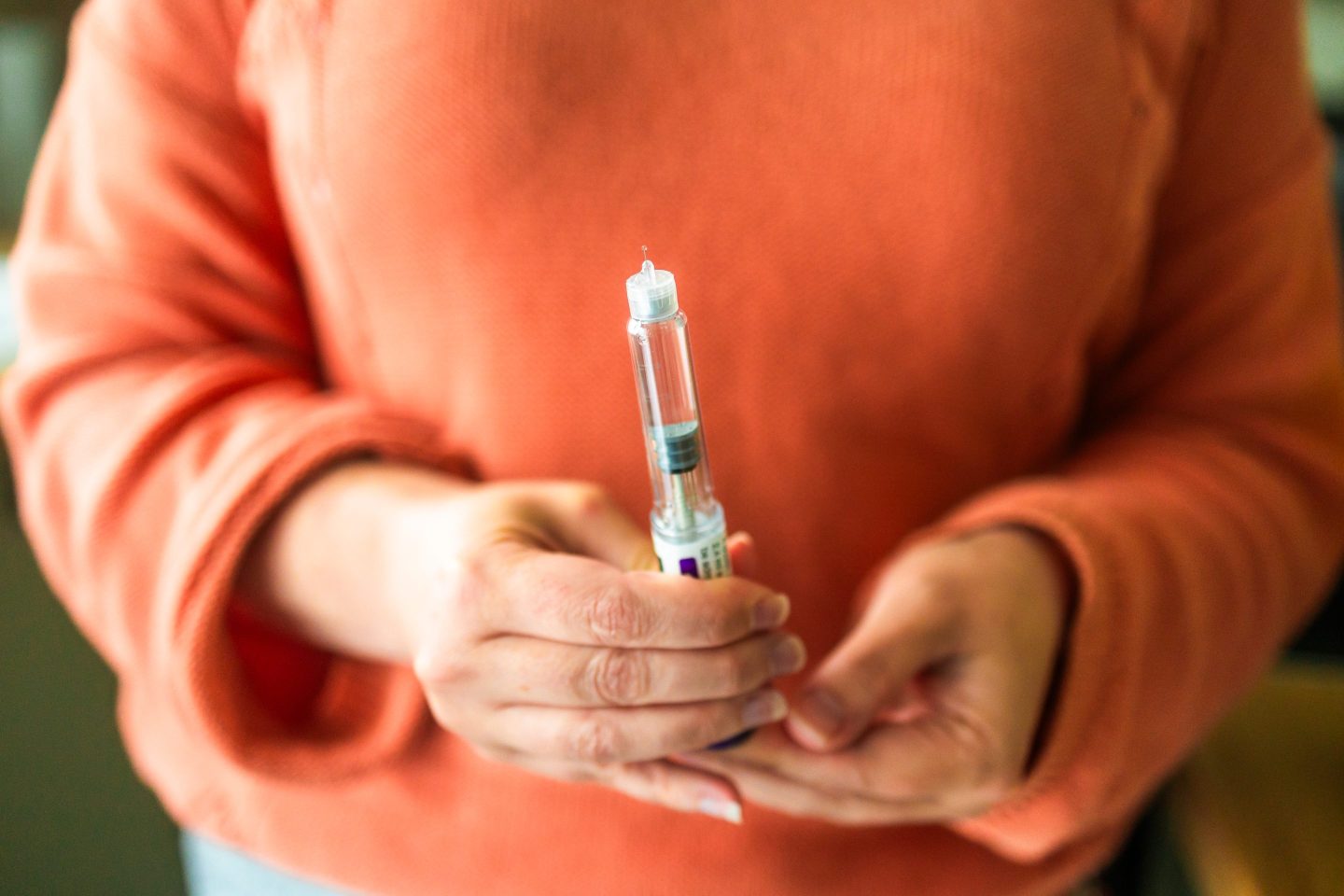 Closeup of woman's torso in orange sweater holding injectable weight-loss drug.