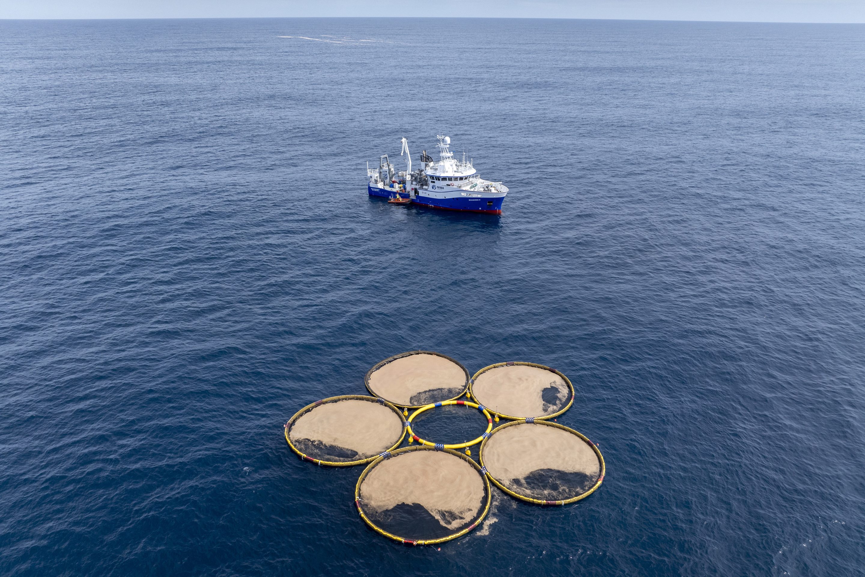 Circular structures called booms containing particles engineered by the company Gigablue, float near a research vessel in the Pacific Ocean off the coast of Dunedin, New Zealand, Saturday, Oct. 19, 2024, as part of a project to grow tiny organisms known as phytoplankton that absorb carbon dioxide from the ocean. 