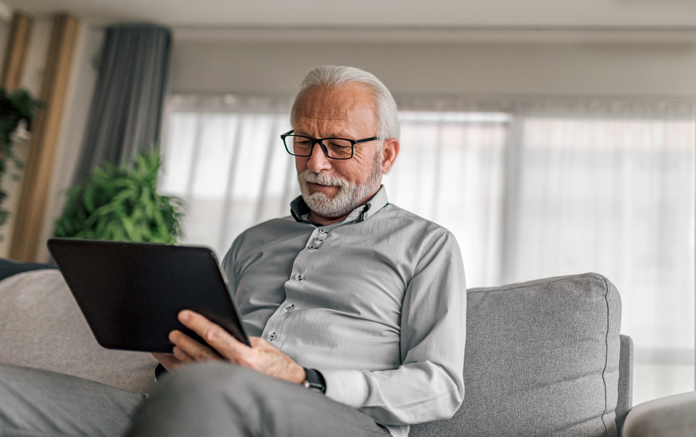 An old man holding a tablet sitting on a couch