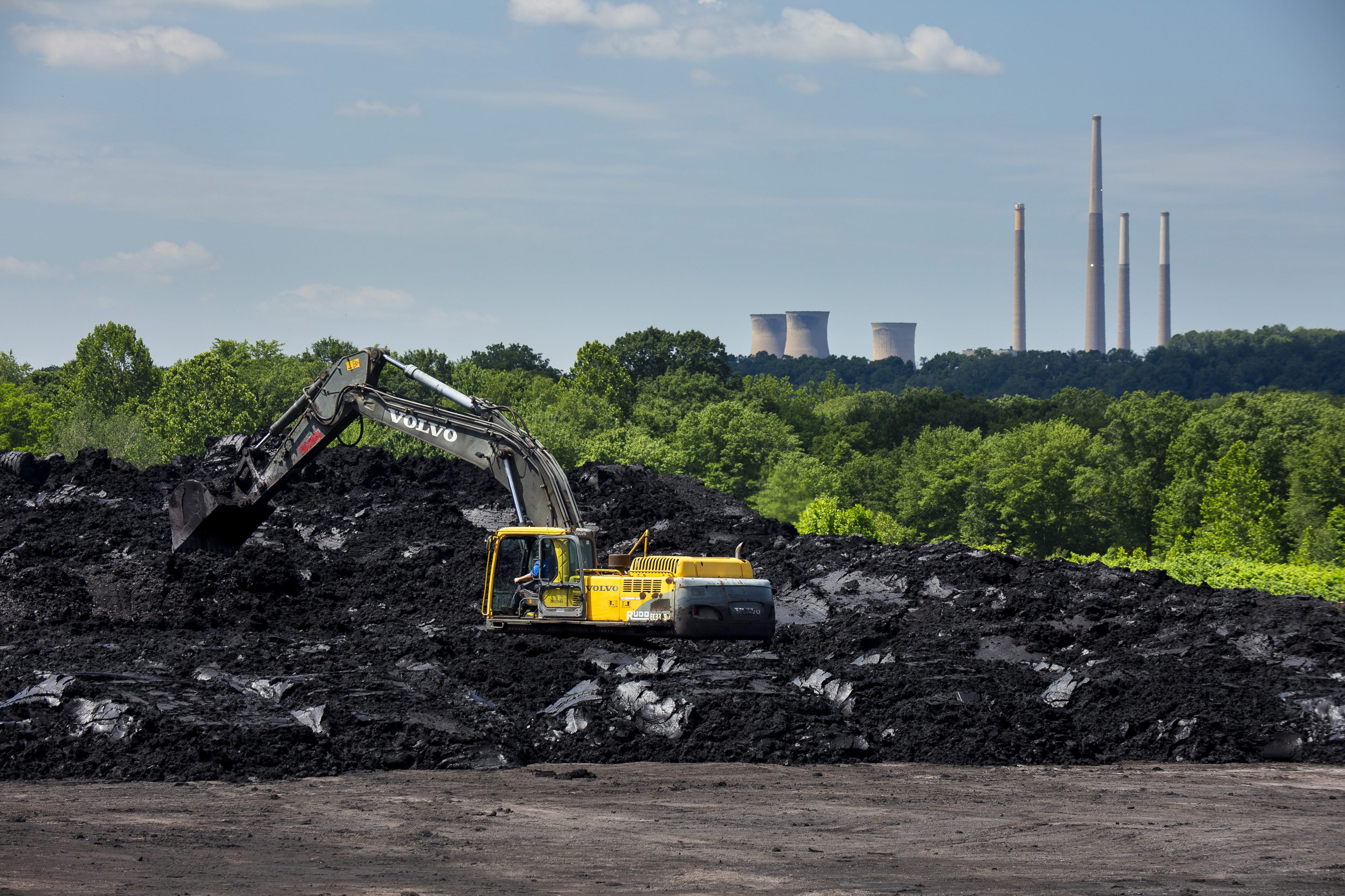 With the shuttered Homer City coal plant in the background, at the Lucerne Reclamation project site in Pennsylvania, a worker moves coal refuse to be prepared for transport to be cleaned on June 12, 2024. The soil, contaminated by coal refuse, is cleaned and returned to the land where it is encased and covered with top soil and planted as a meadow.