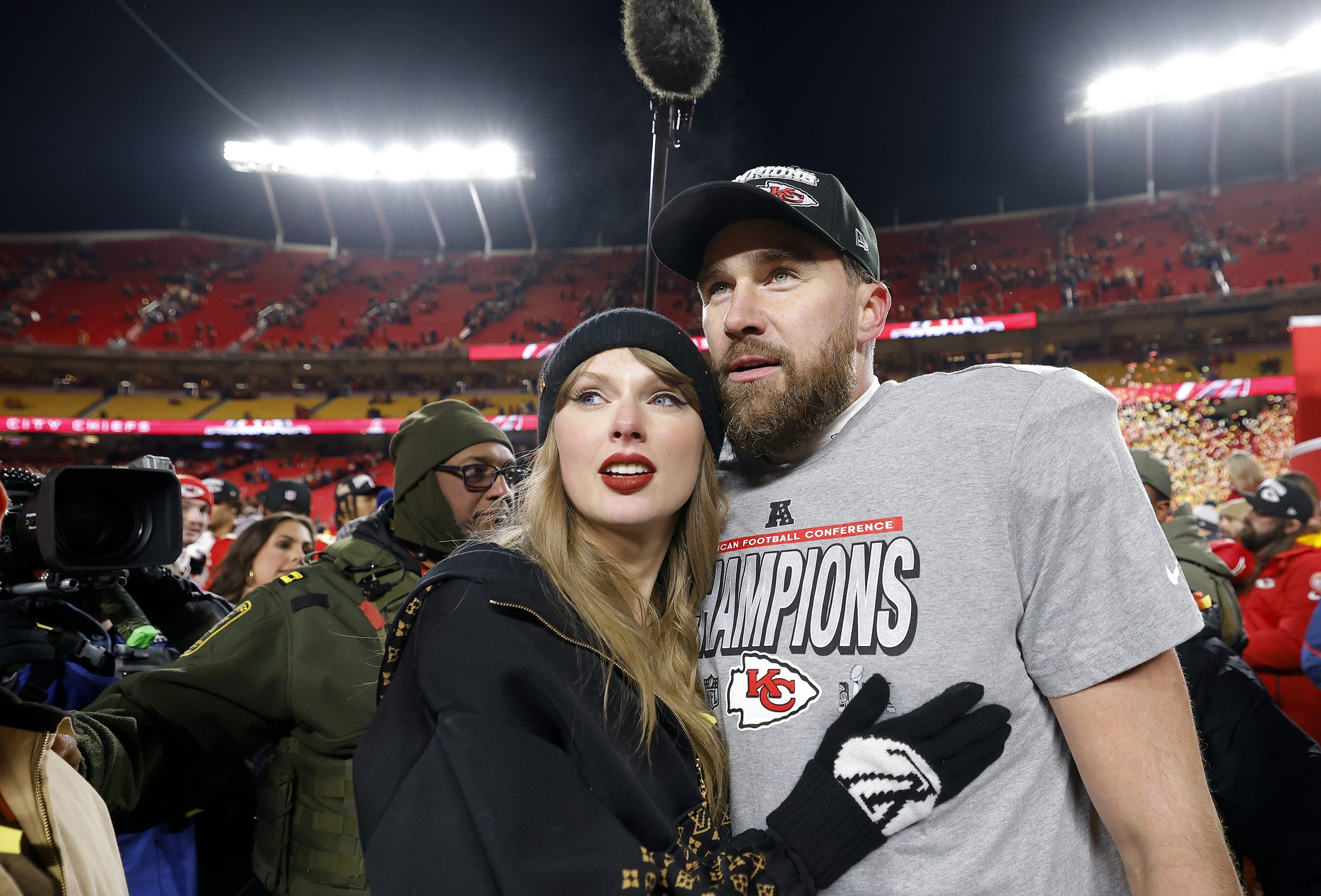 Taylor Swift hugs her boyfriend Travis Kelce on the field, wearing gloves and red lipstick.
