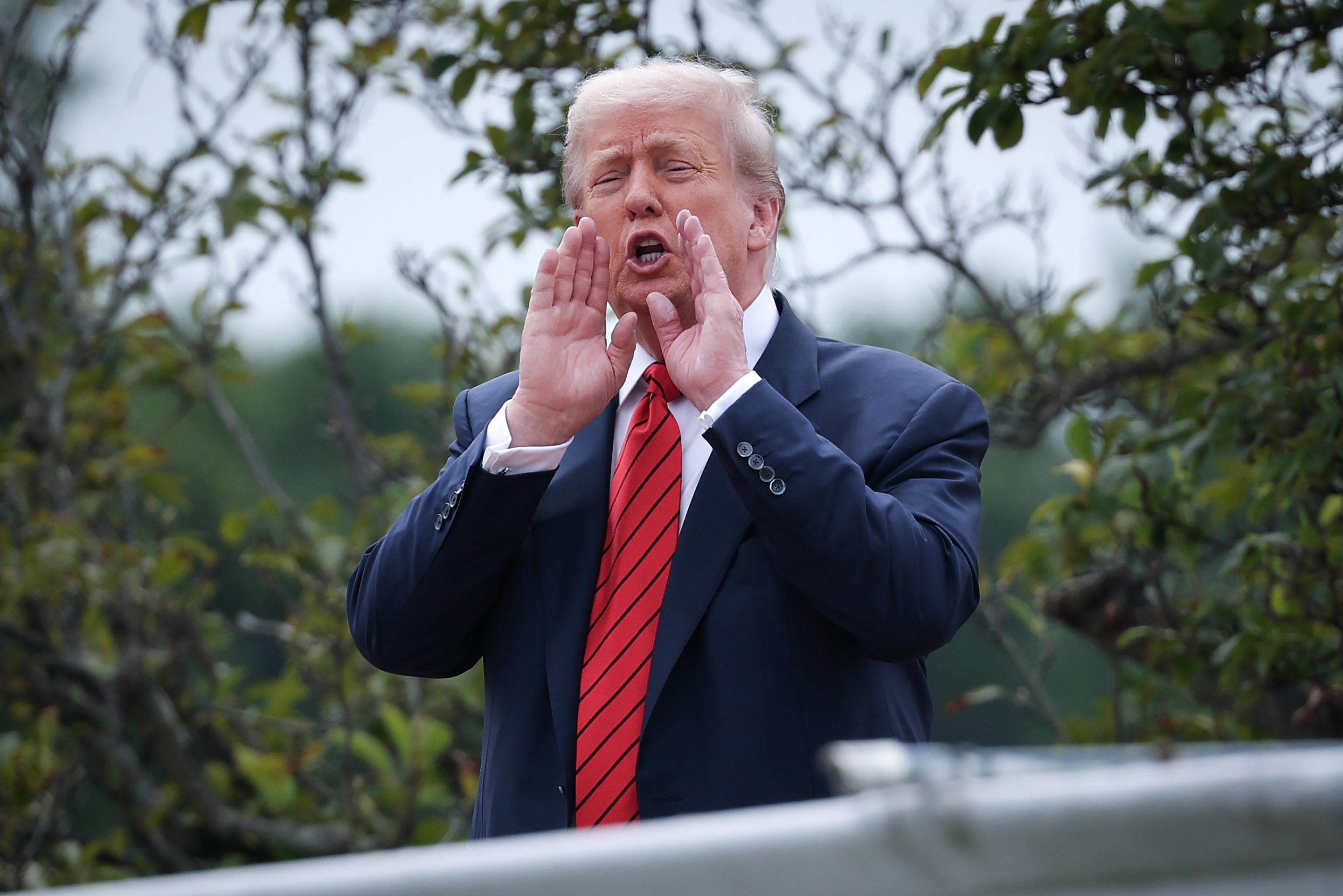President Donald Trump shouts answers to questions from reporters as he tours the roof of the West Wing of the White House on Tuesday.