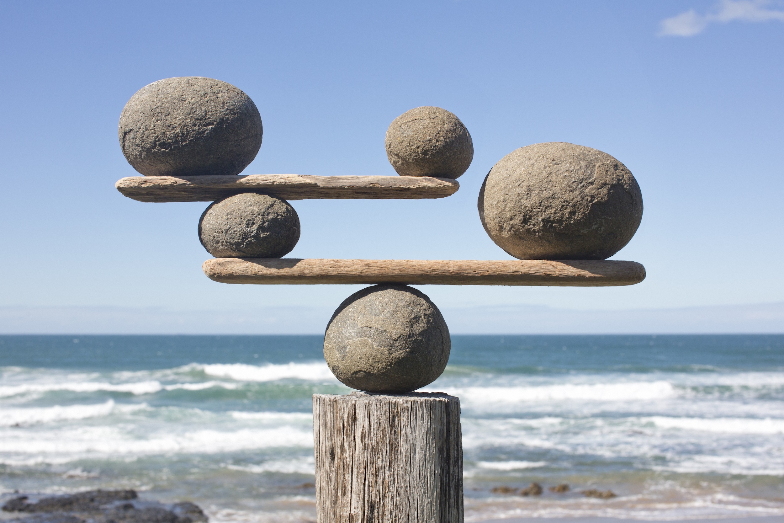 Photo: Rocks balancing on driftwood, sea in background.