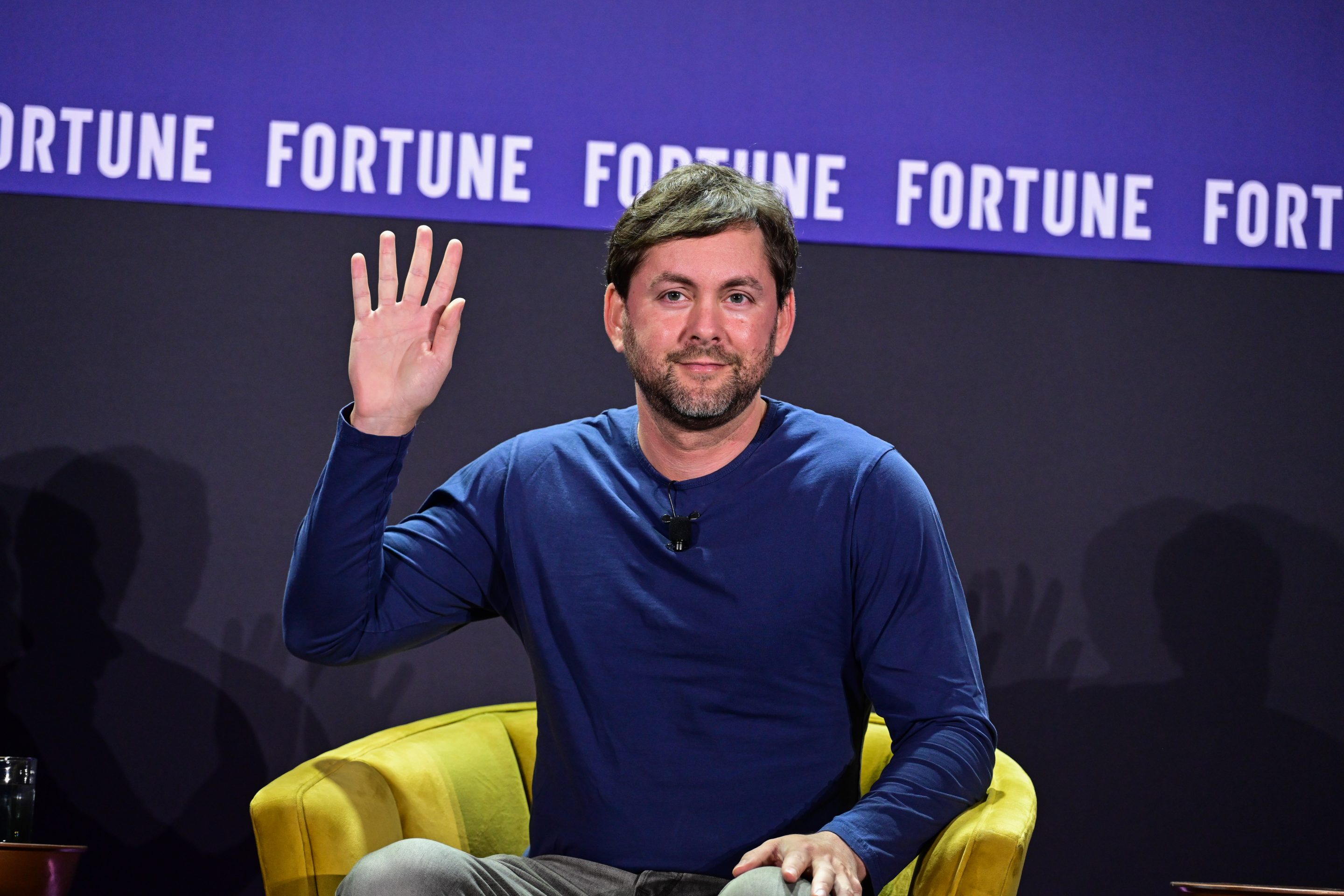 Jesse Levinson sits in a yellow chair in front of a purple "Fortune" background. He is waving with his right hand.