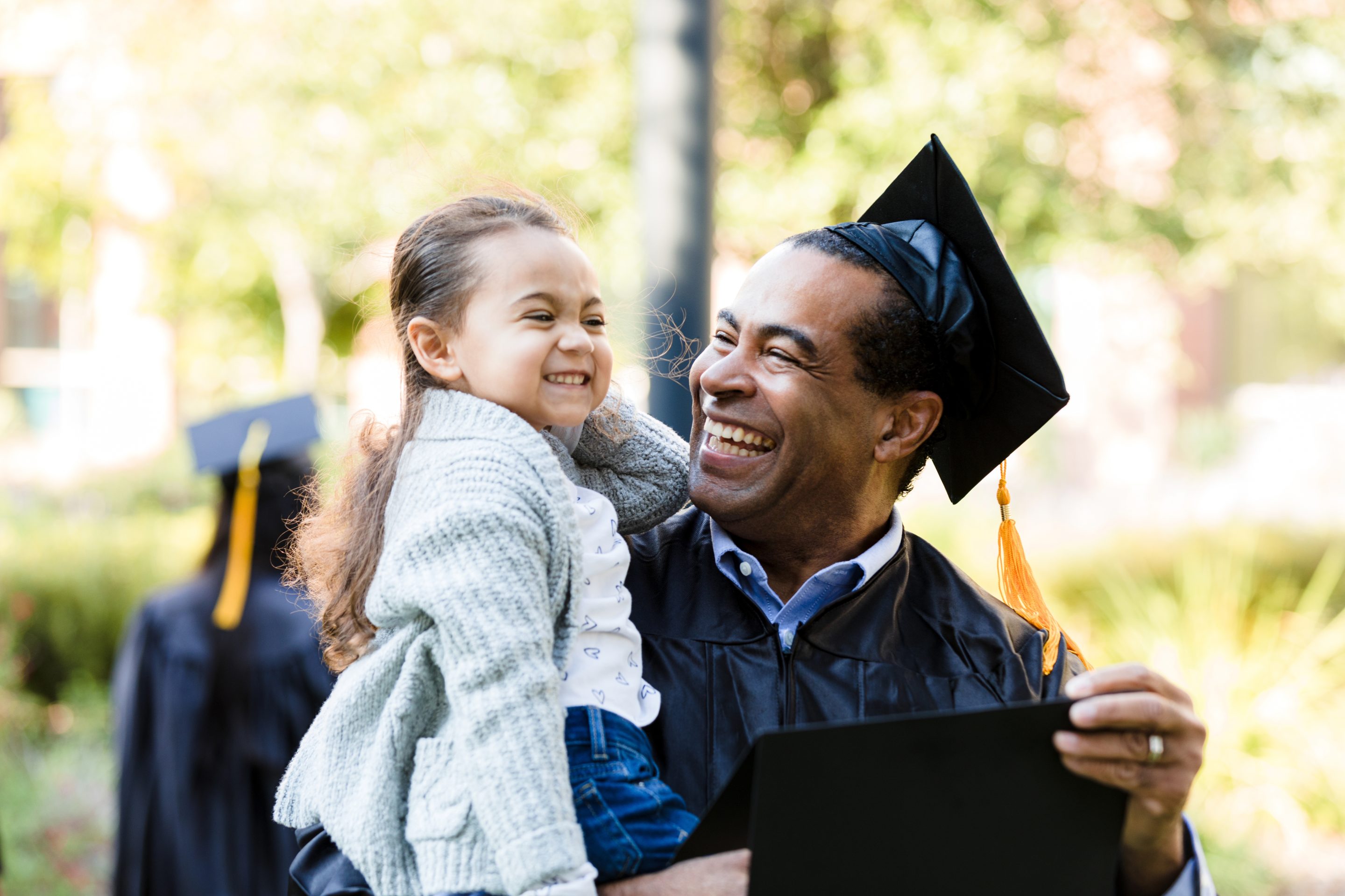 Little girl held in the arms of a man wearing a graduation cap and gown