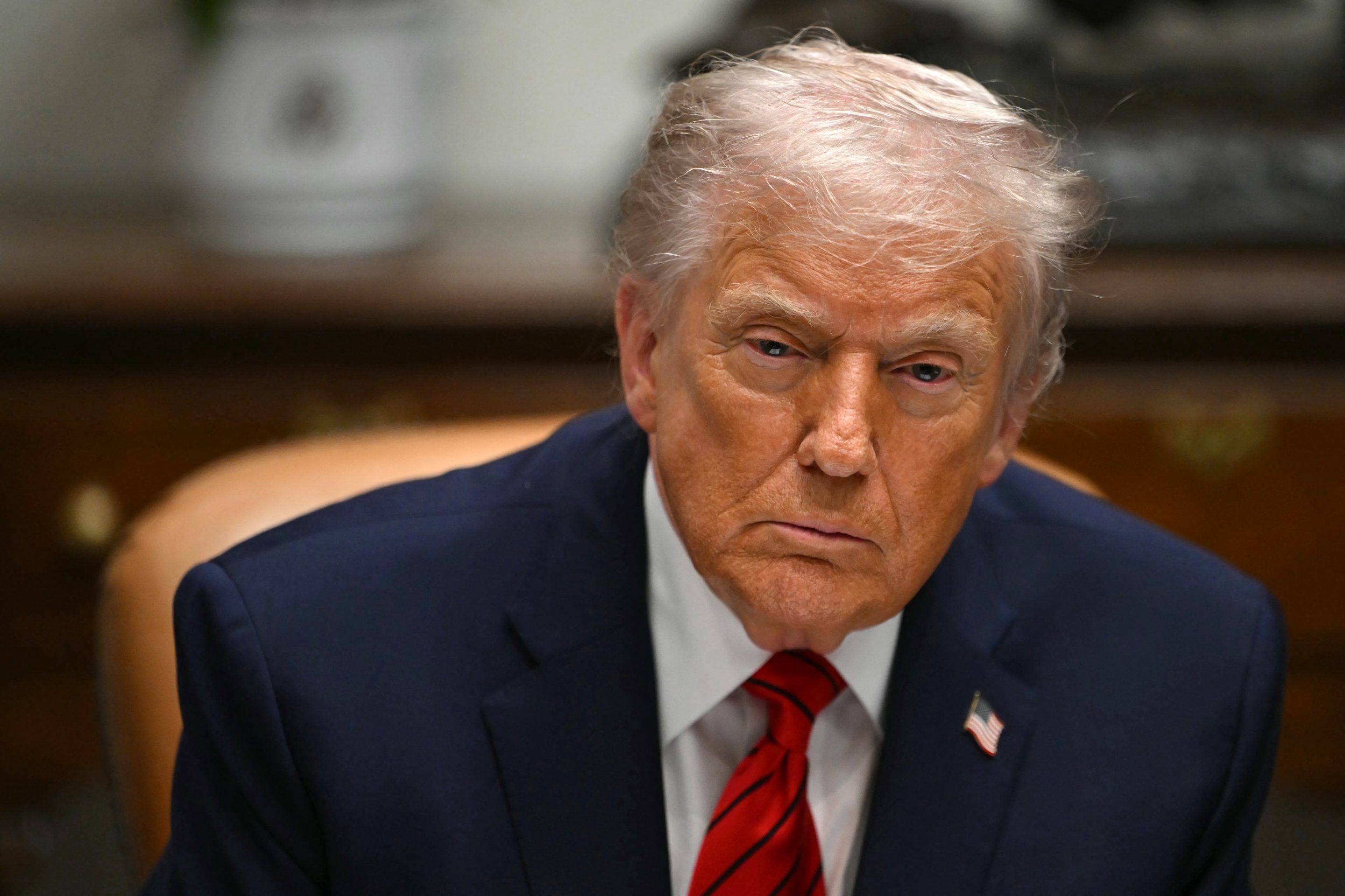 Donald Trump, sitting in the Roosevelt Room, looks forward and frowns.
