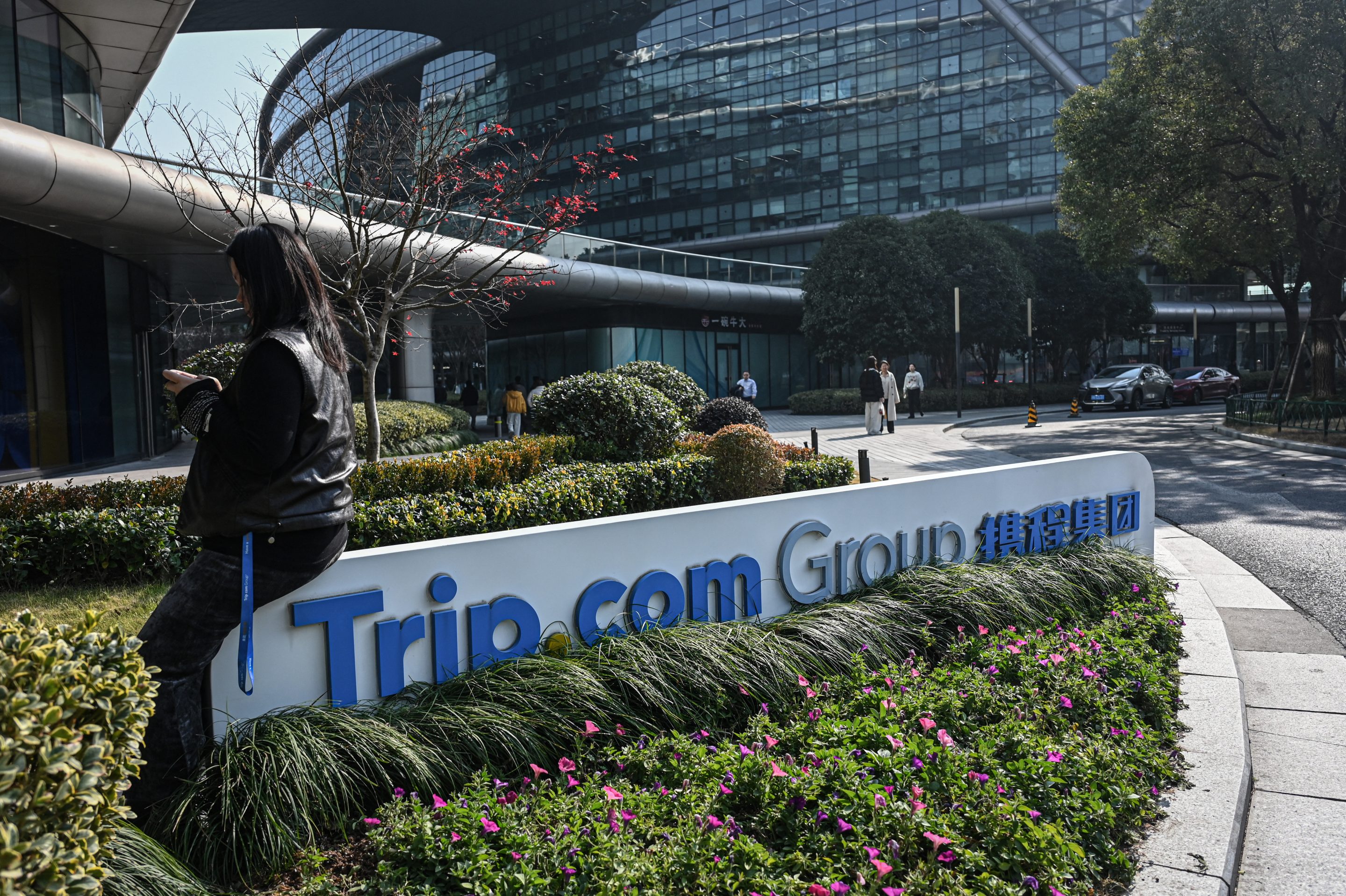 A woman sits on a signage of China's travel agency Trip.com Group at its headquarters in Shanghai on January 15, 2026. 