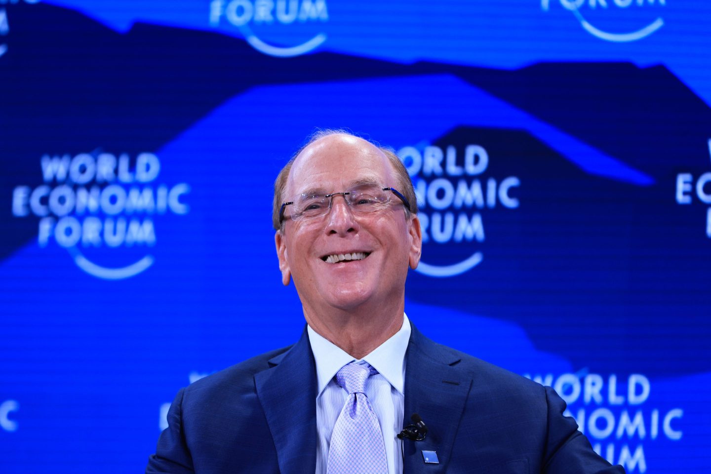 Man with glasses smiling before a blue background.