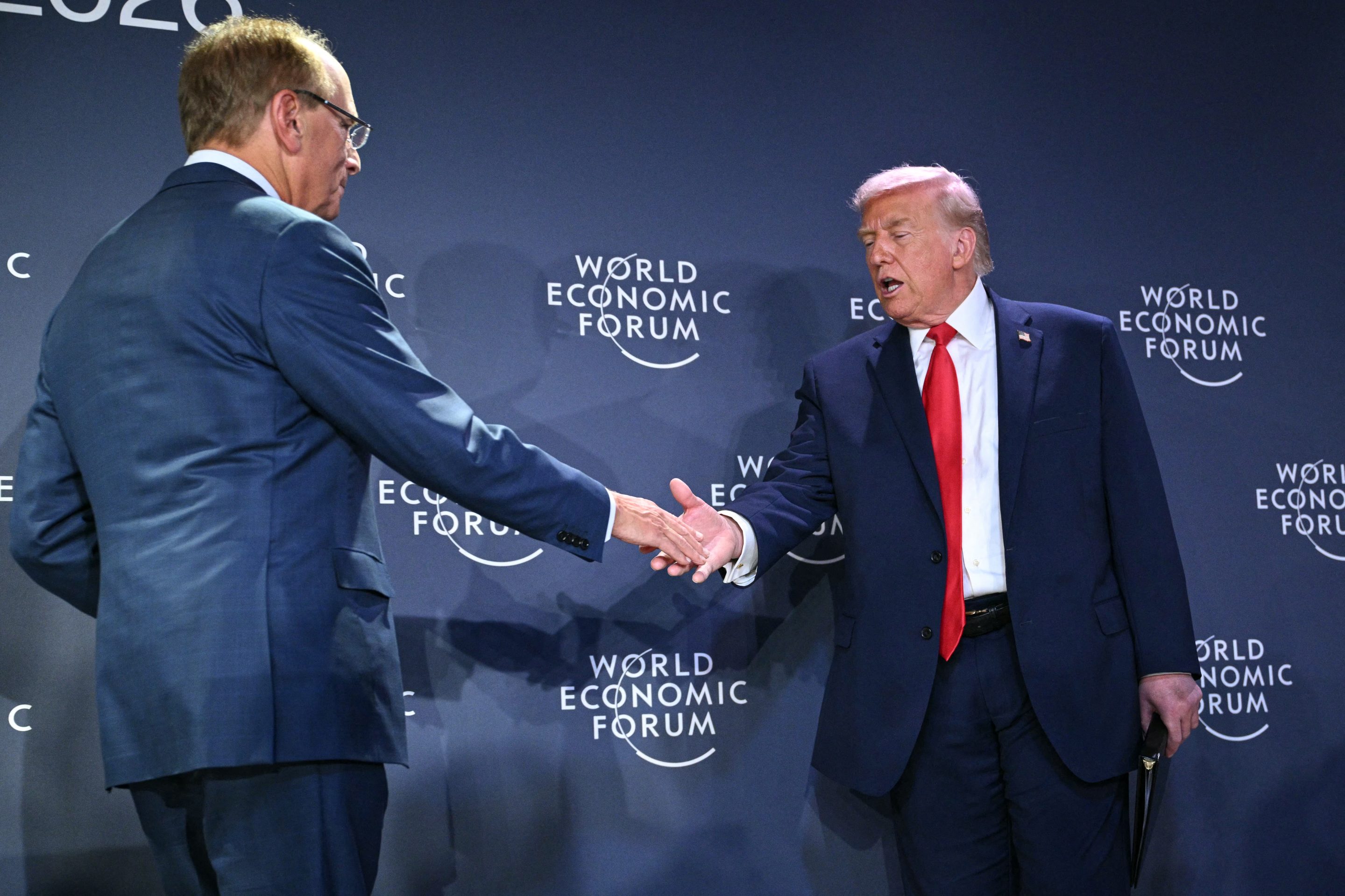 US President Donald Trump (R) shakes hands with BlackRock chairman and WEF co-chairman Larry Fink during a reception with business leaders on the sidelines of the World Economic Forum (WEF) annual meeting in Davos on January 21, 2026.