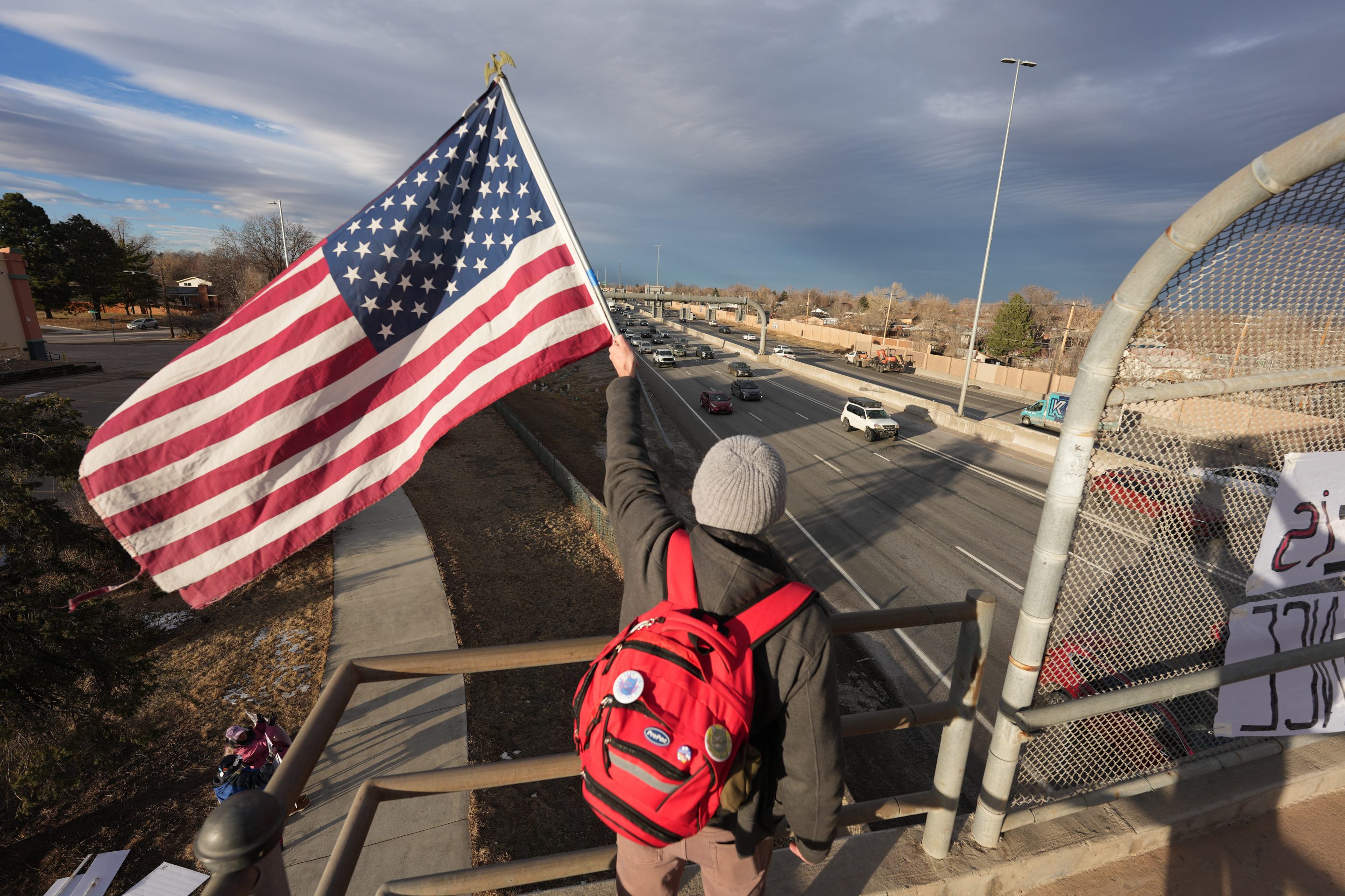 A protester holds American flag while waving at motorists Wednesday, Jan. 28, 2026, from an overpass along Interstate 25 in Northglenn, Colo. 