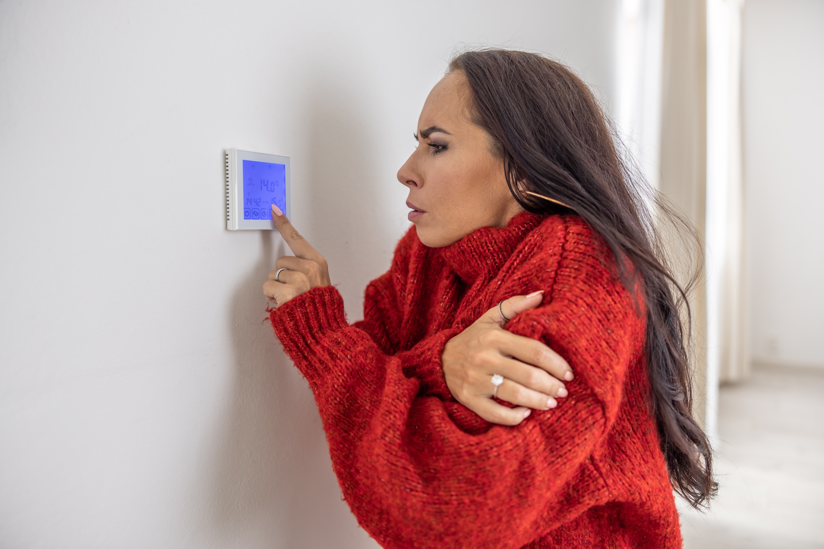 Photo of woman in a sweater operating a thermostat
