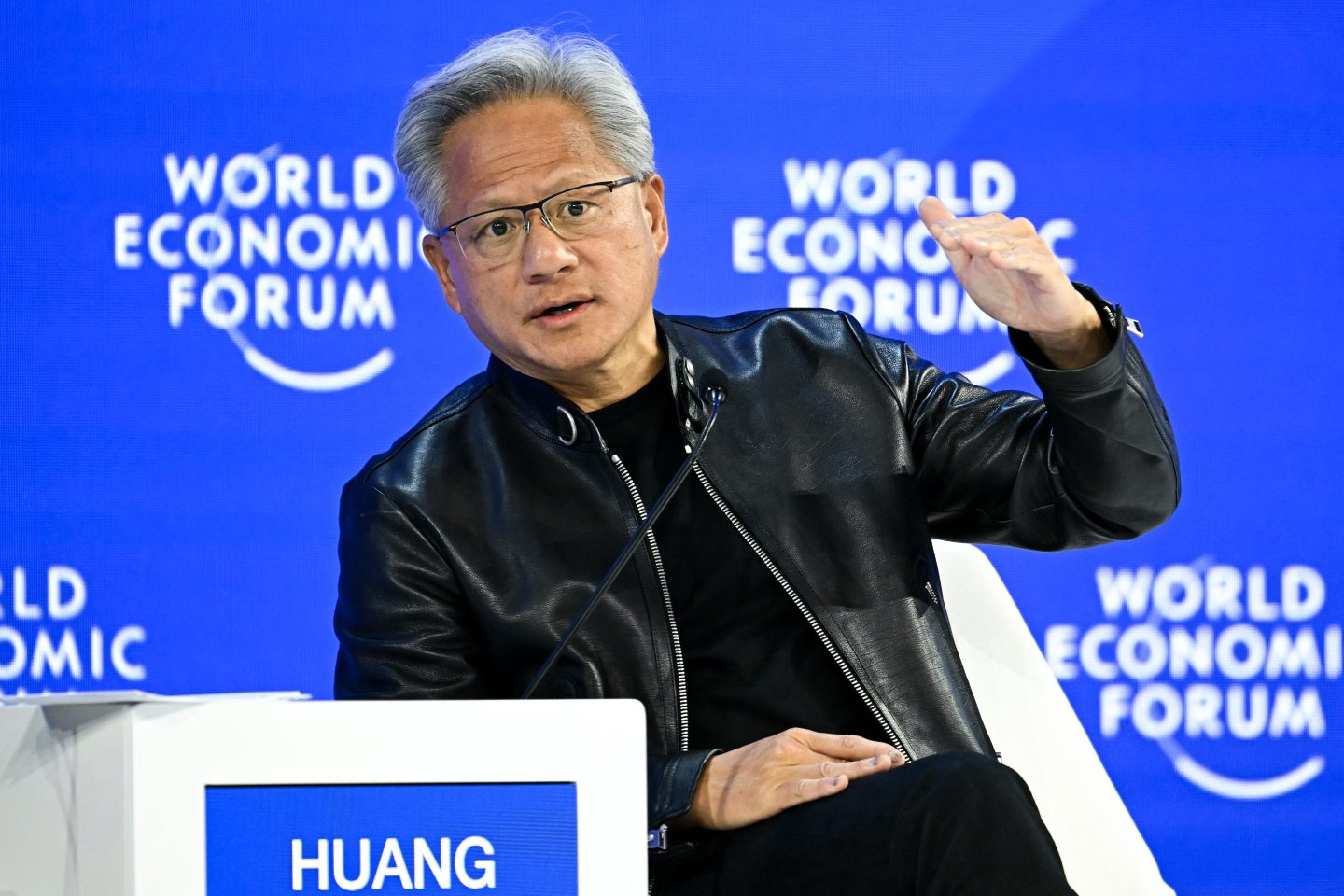 Seated man in black jacket in front of a blue background