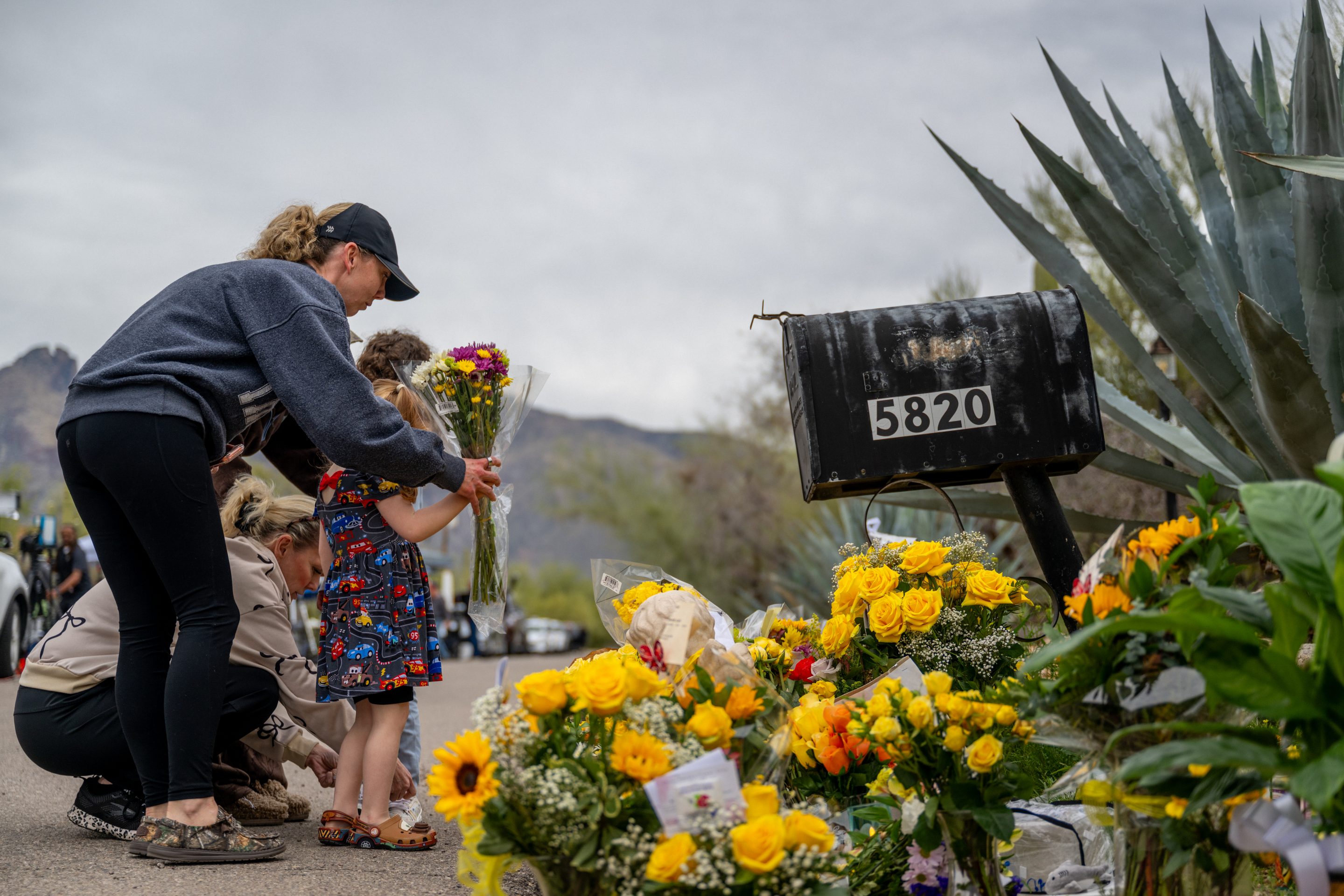A woman and girl put flowers down in front of Nancy Guthrie’s home