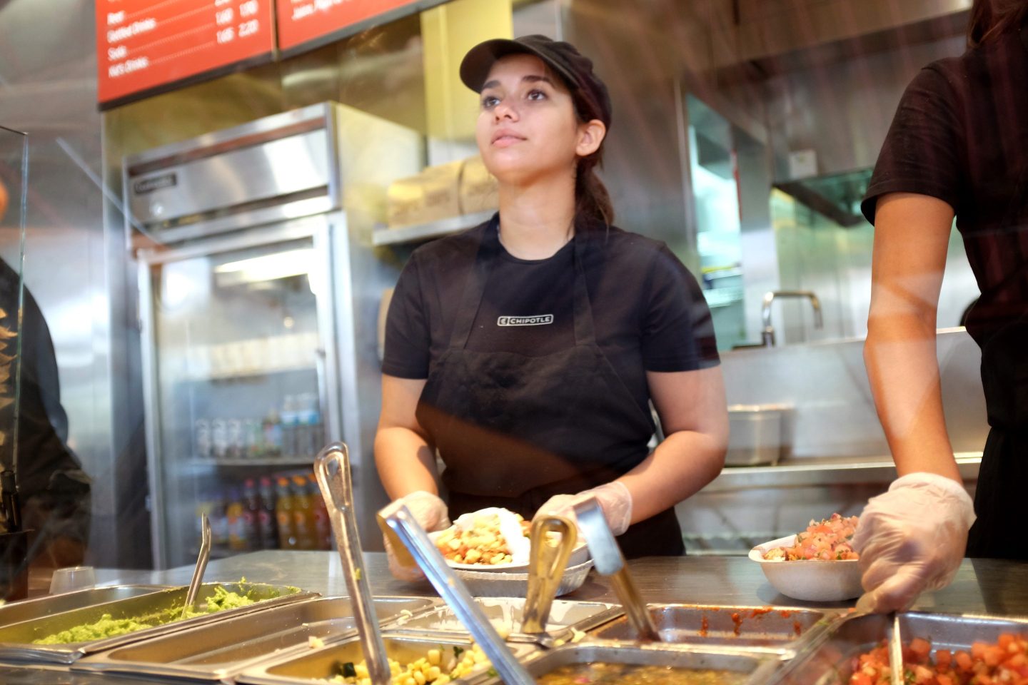 A Chipotle server looks up as she stands behind the counter holding a burrito bowl.