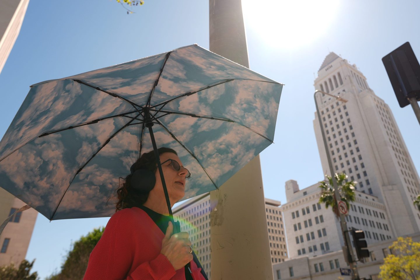 A pedestrian holds a cloud themed umbrella under a sunny day