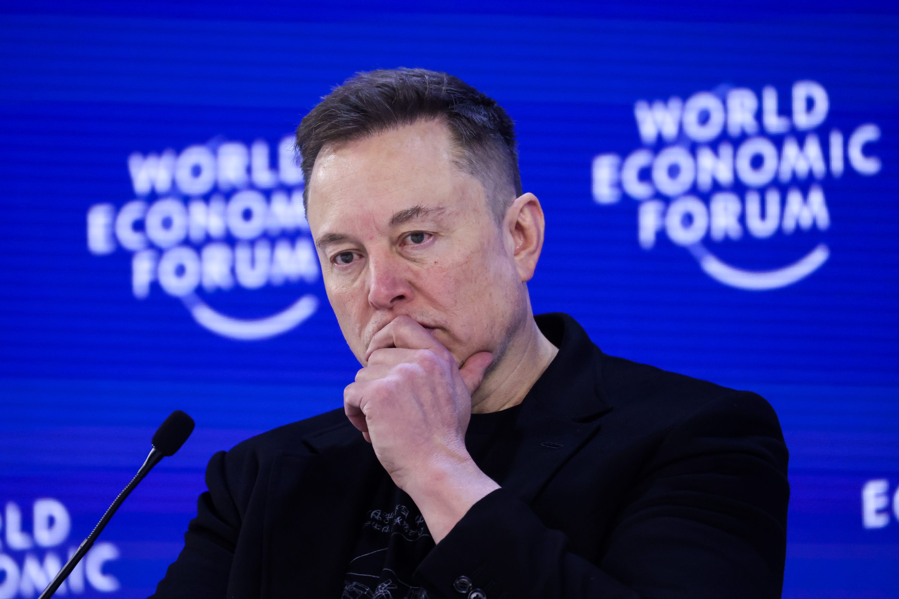 Elon Musk looks down with one hand pressed to his mouth.