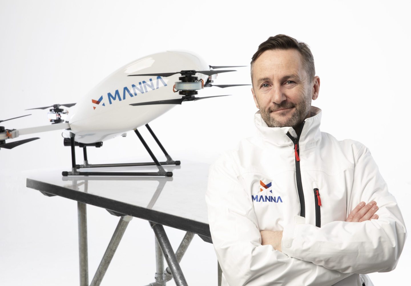 Bobby Healy stands in front of a Manna drone with his arms crossed.
