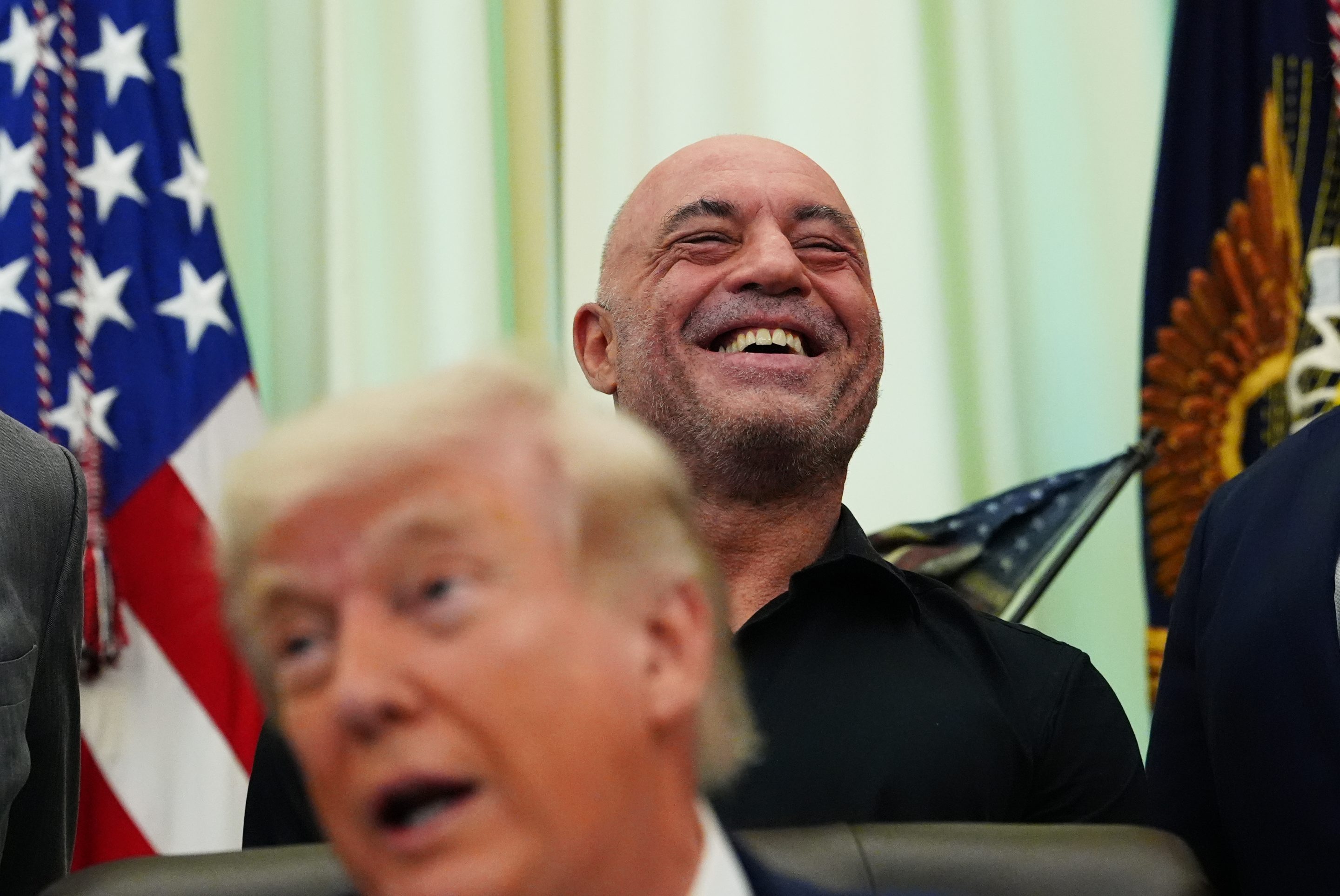 Joe Rogan laughs as President Donald Trump speaks in the Oval Office of the White House, Saturday, April 18, 2026.