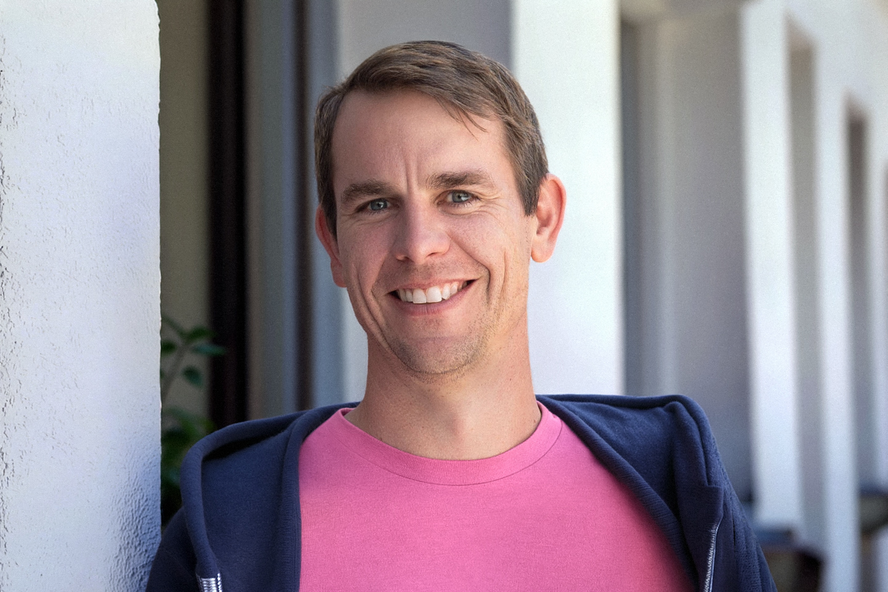 Colin Zima smiles while wearing a pink shirt