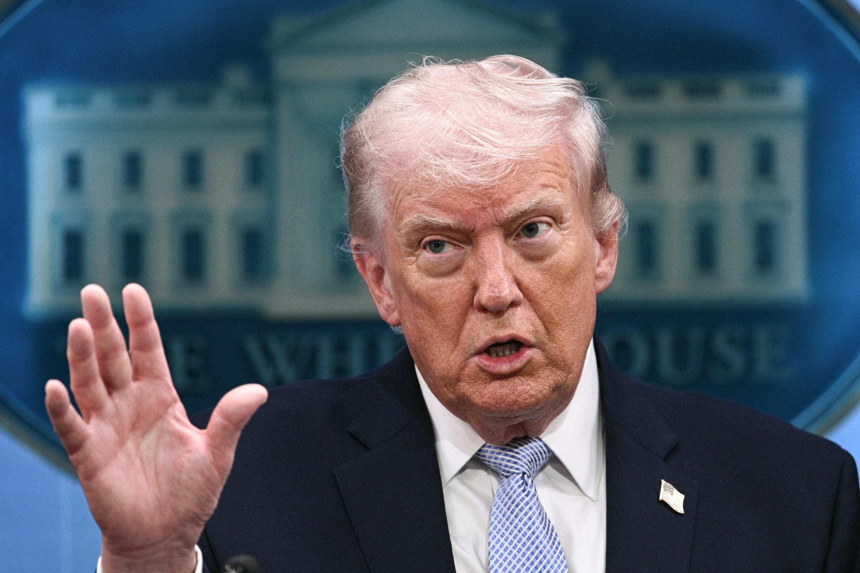 Donald Trump speaks and puts one hand in the air while standing in the Press Briefing Room.