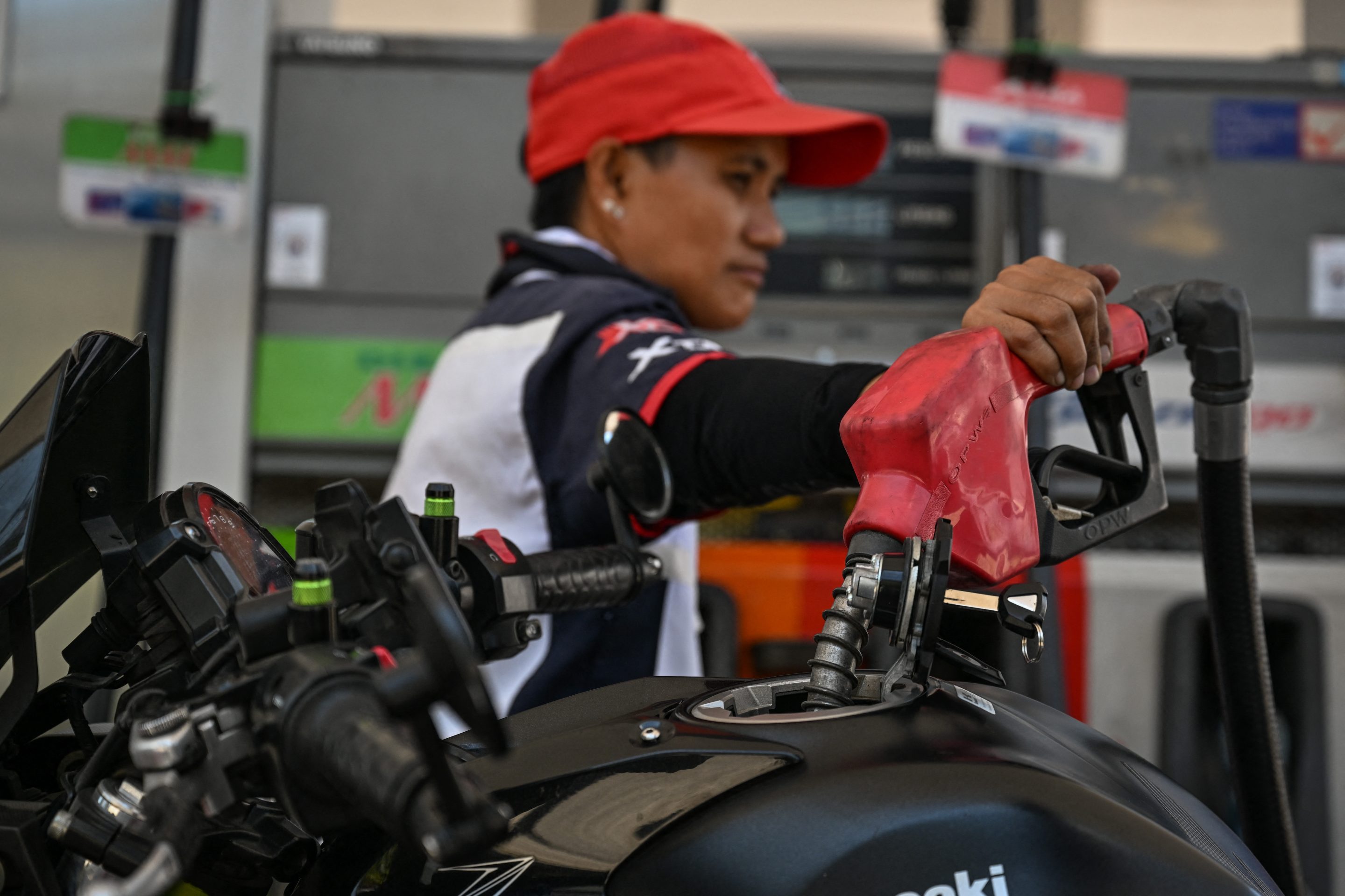 A person wearing a red hat has their hand on a gas pump.