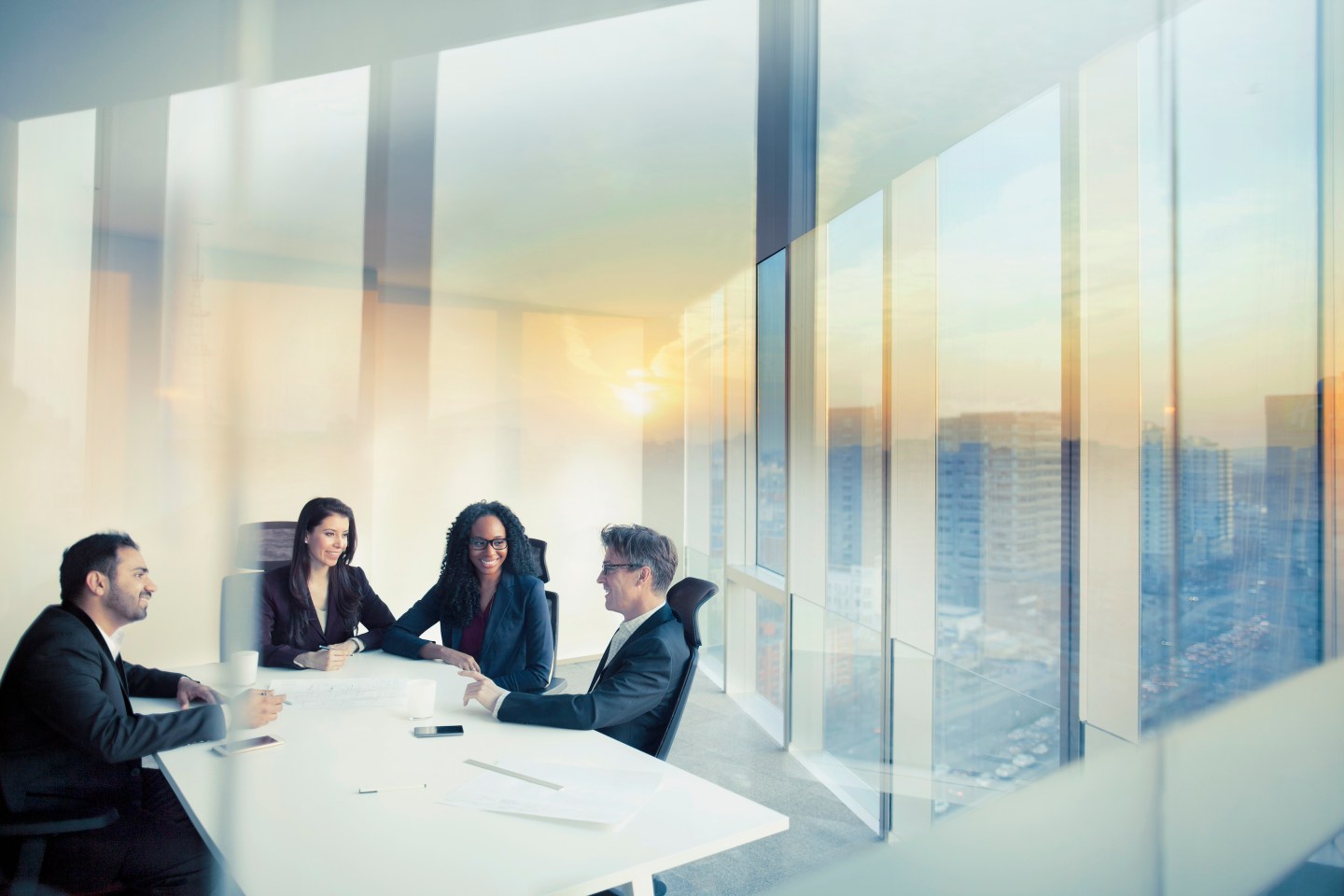 Senior executive team together in conference meeting room in contemporary modern office bright sunny daylight sunset dusk talking discussing planning organizing strategy.