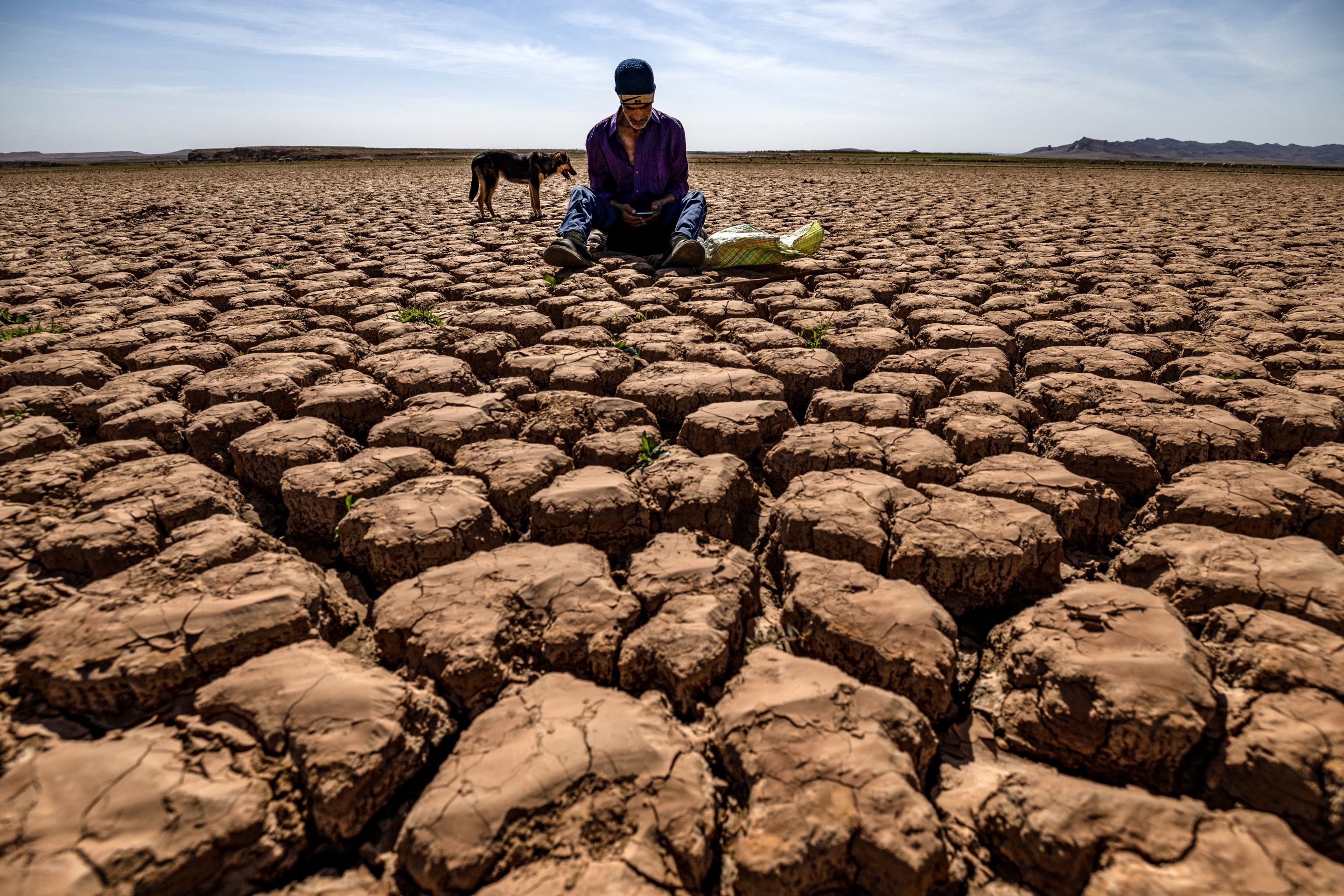 A shepherd checks his mobile phones sitting on cracked earth at al-Massira dam in Ouled Essi Masseoud village, some 140 kilometres (85 miles) south of Casablanca, on March 6, 2024.