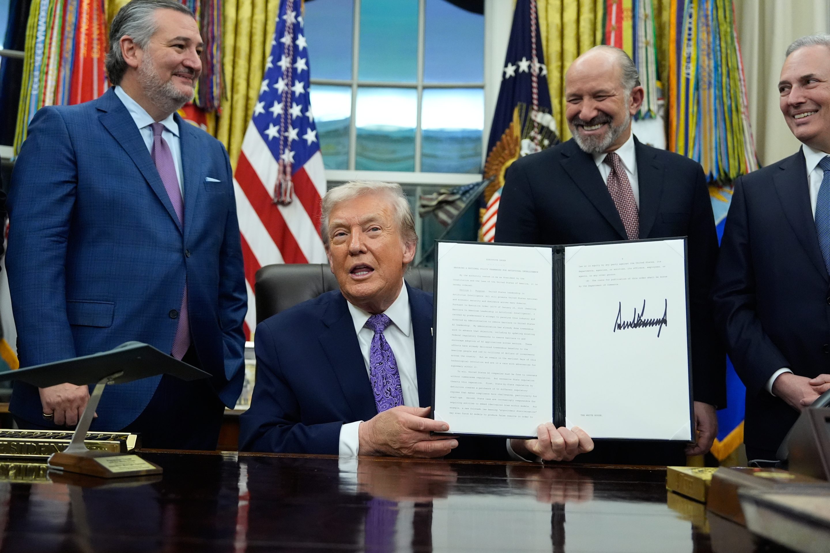 Flanked by Sen. Ted Cruz, R-Texas, left, Secretary of Commerce Howard Lutnick, second right, and White House AI and Crypto Czar David Sacks, President Donald Trump displays his signed AI initiative in the Oval Office of the White House, Dec. 11, 2025.