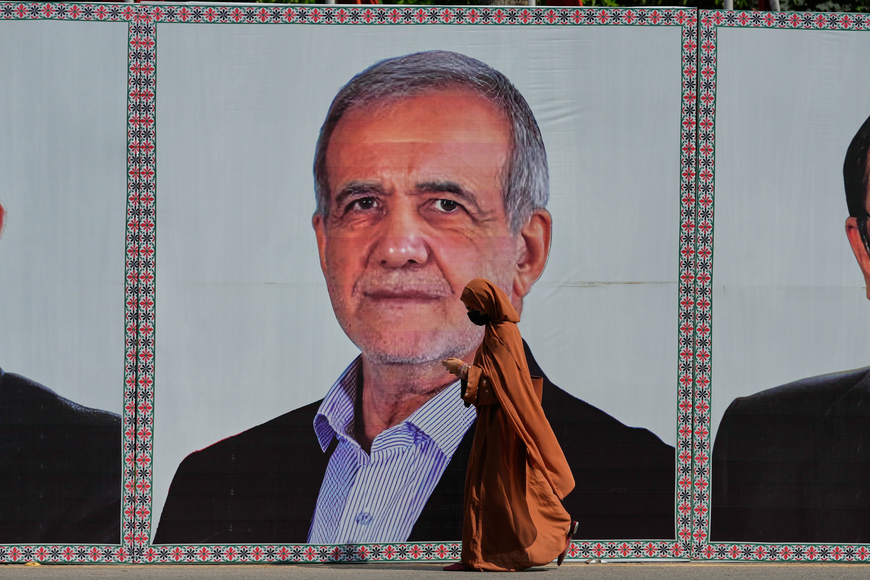 A woman walks past a welcoming billboard featuring Iranian President Masoud Pezeshkian along a roadside in Islamabad, Pakistan, Tuesday, June 23, 2026. 