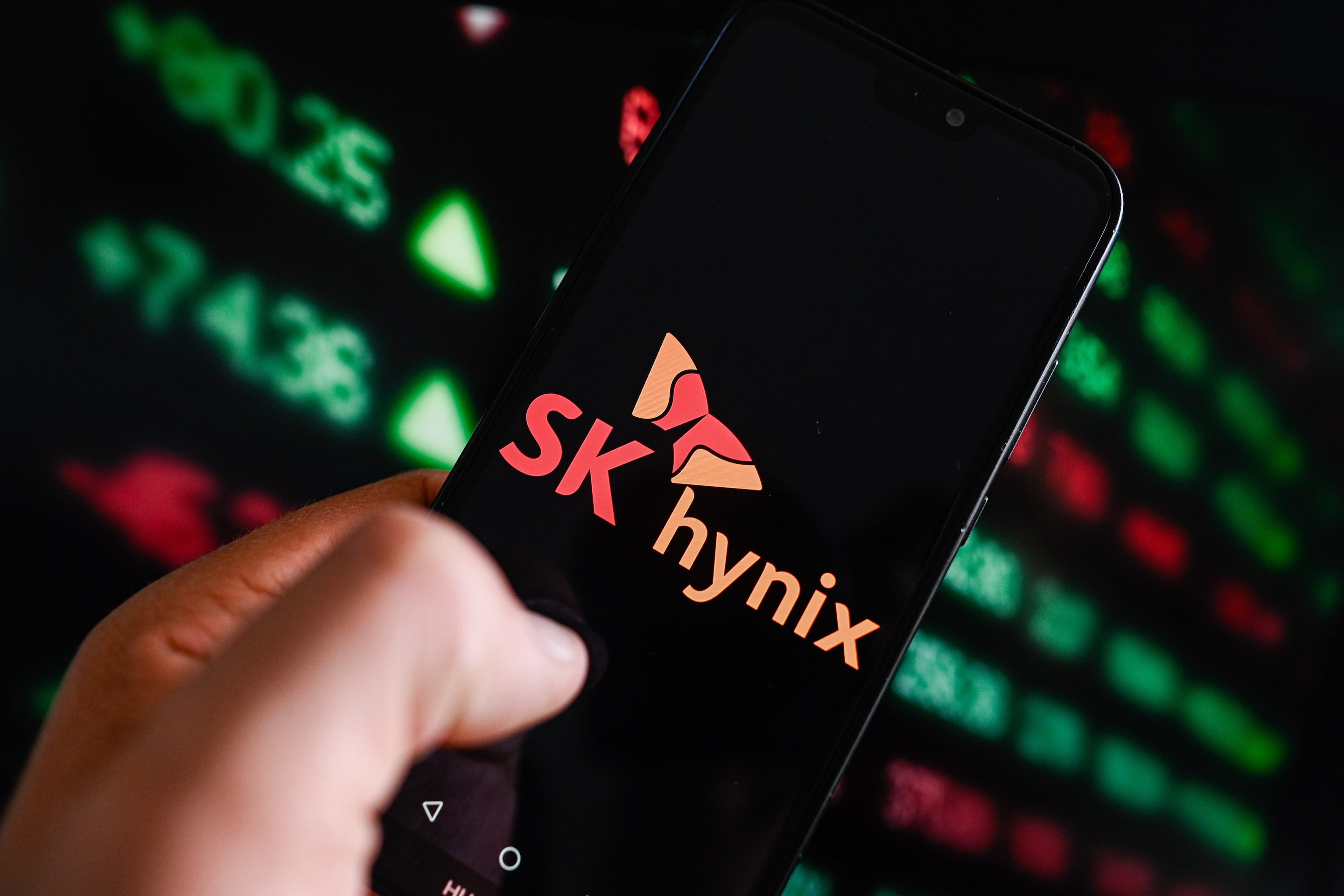In this photo illustration, a Sk Hynix logo is displayed on a smartphone with stock market percentages in the background.