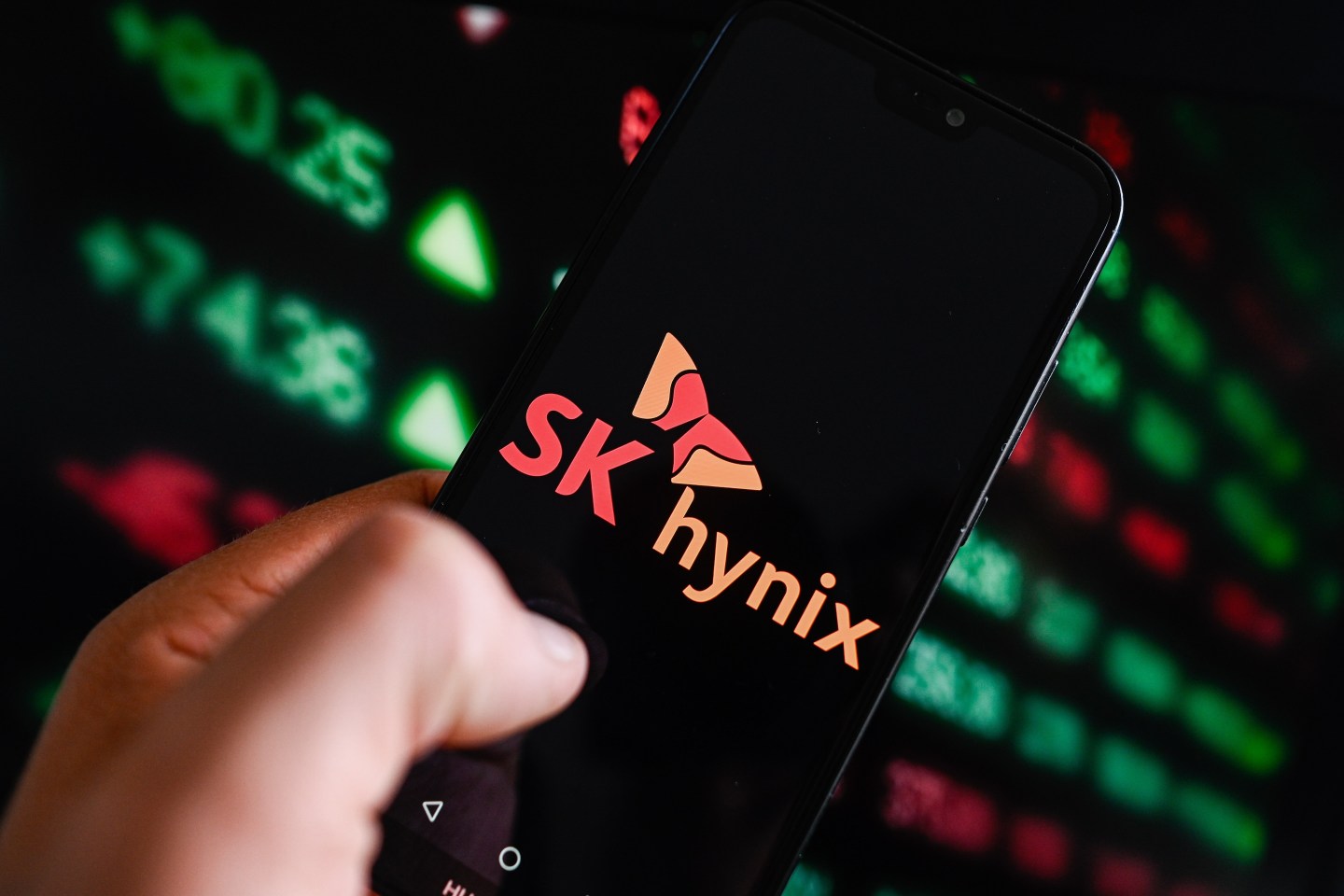 In this photo illustration, a Sk Hynix logo is displayed on a smartphone with stock market percentages in the background.