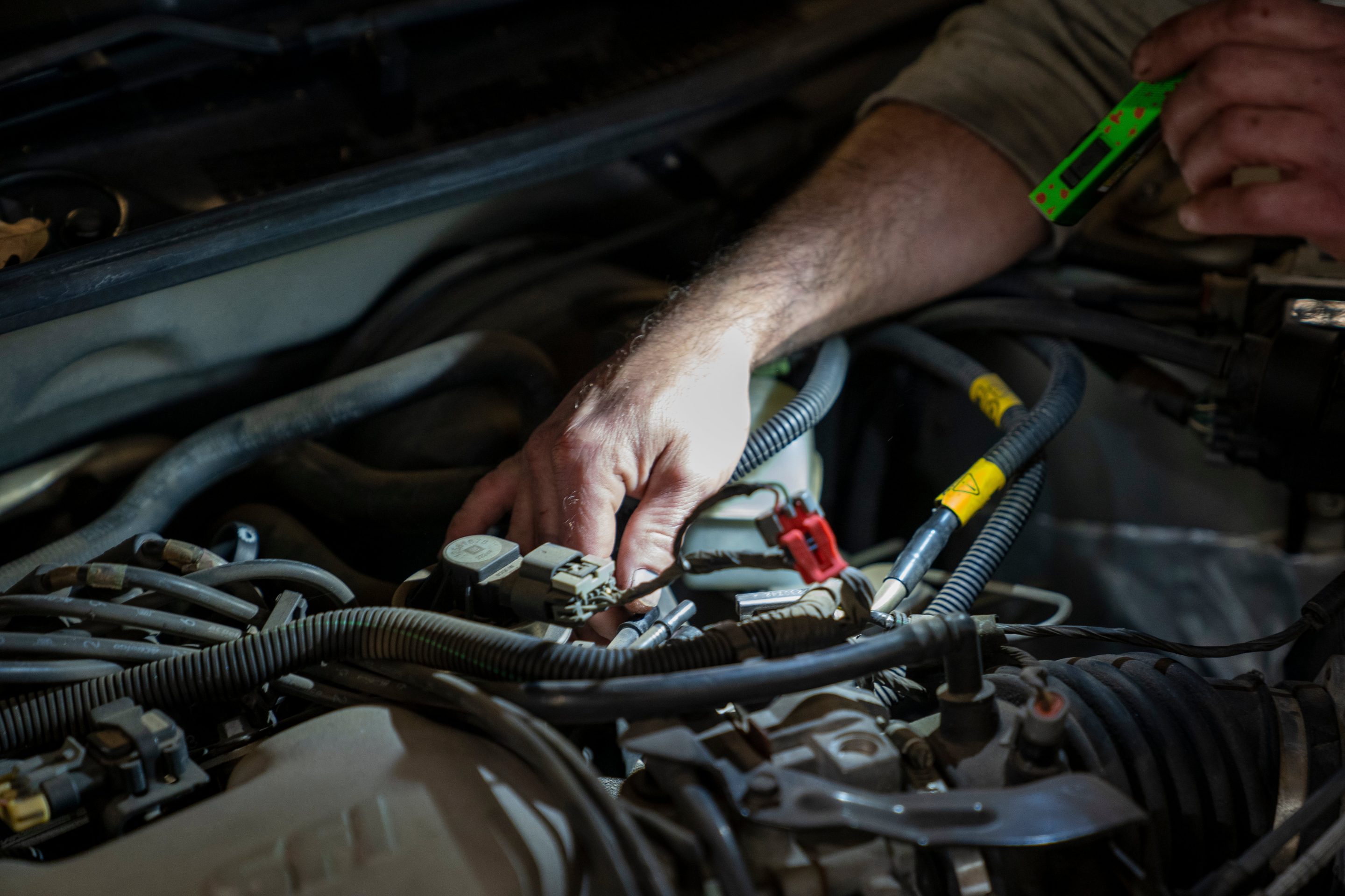 A mechanic uses a flashlight to inspect a vehicle's engine at an automotive shop.