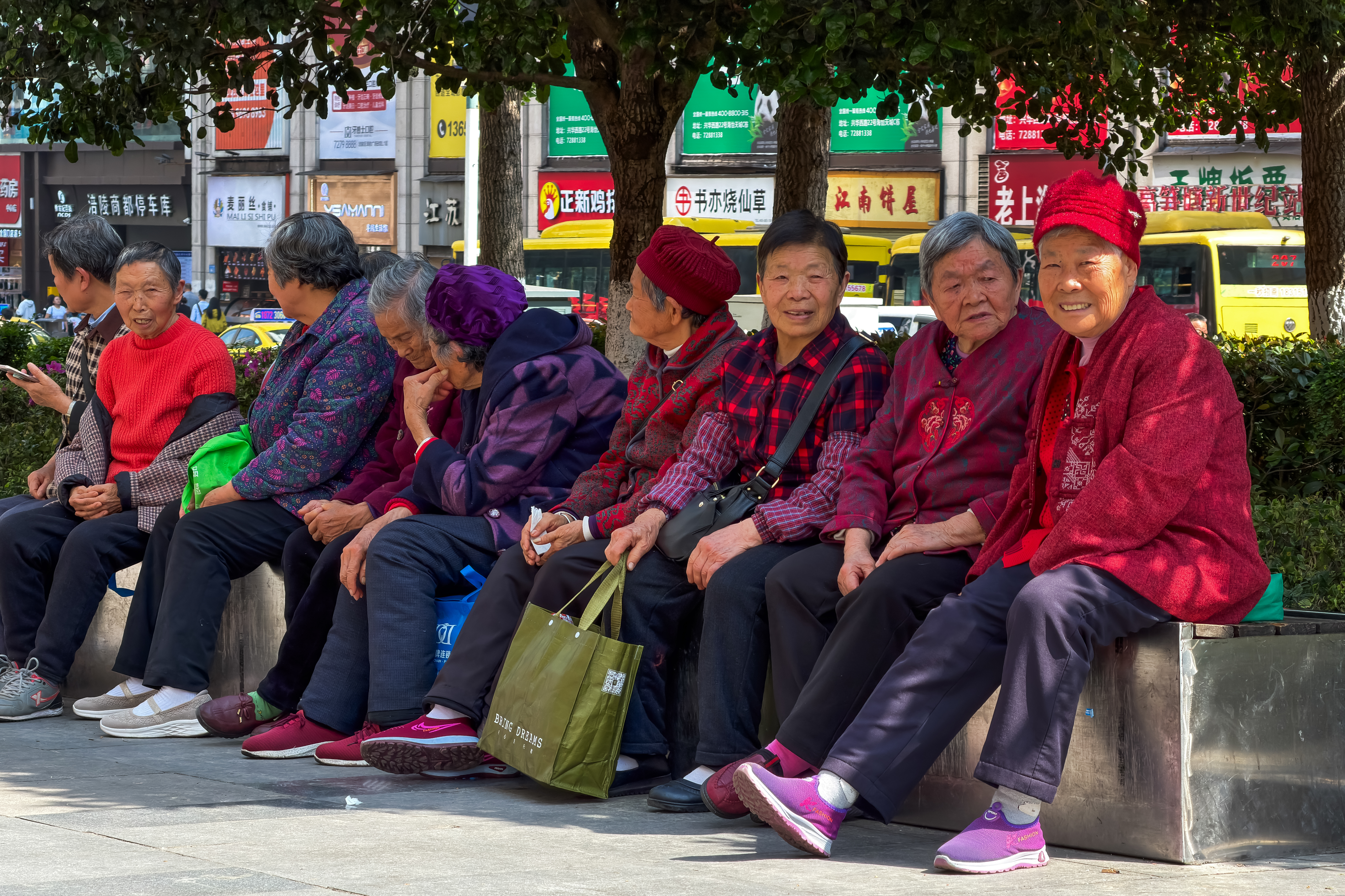 Elderly women sit together along a street under the shade of trees, chatting and resting on April 4, 2026, in Chongqing, China.
