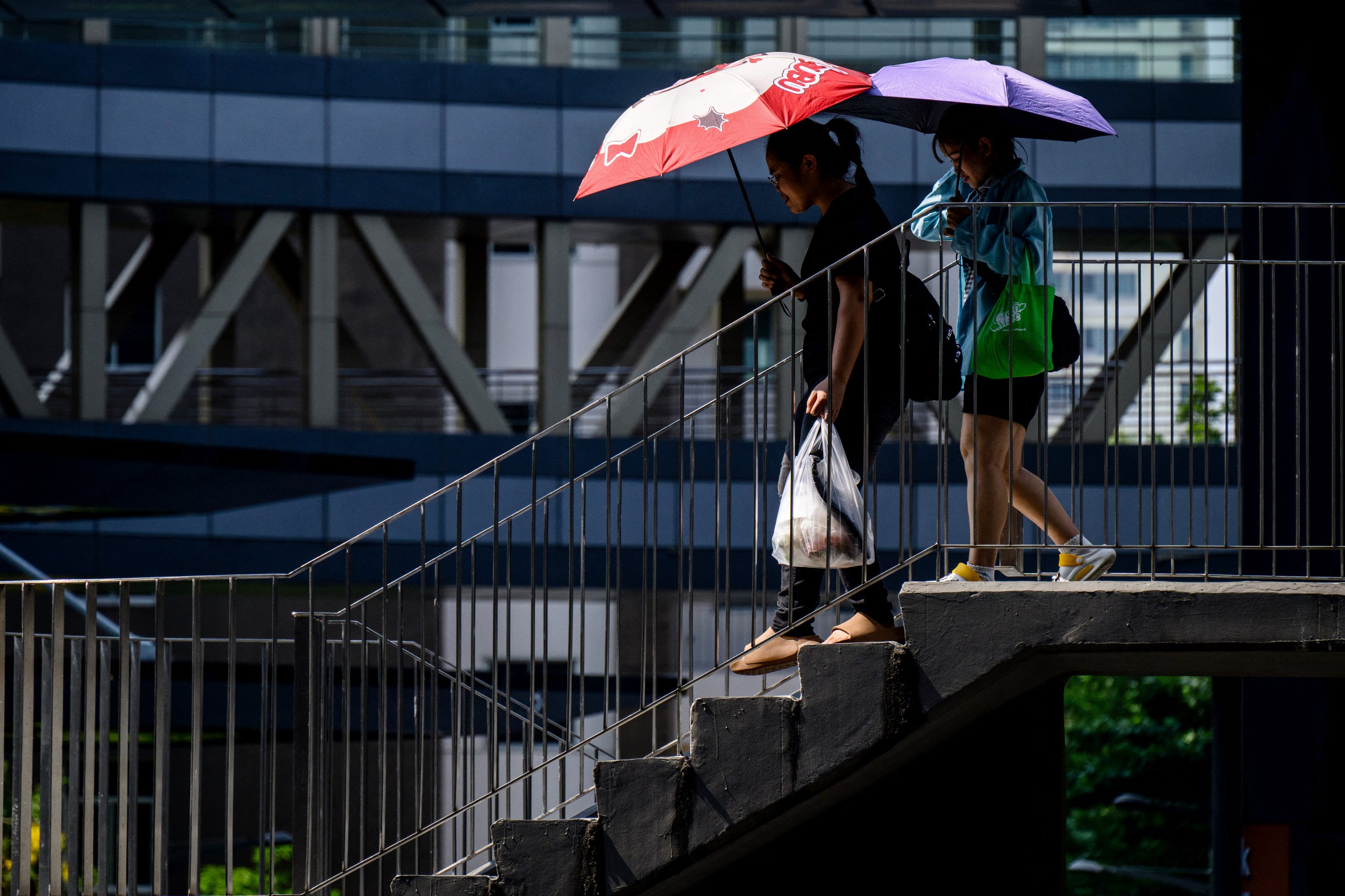 Women use umbrellas to shield themselves from the sun as they walk down a footbridge in Bangkok on April 29, 2026.