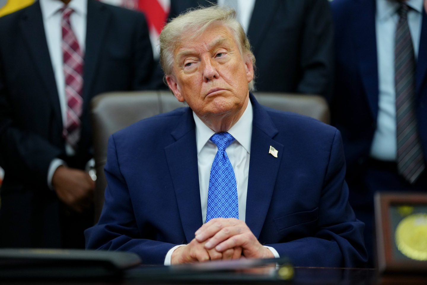 US President Donald Trump sits in silence with his hands folded on top of each other.