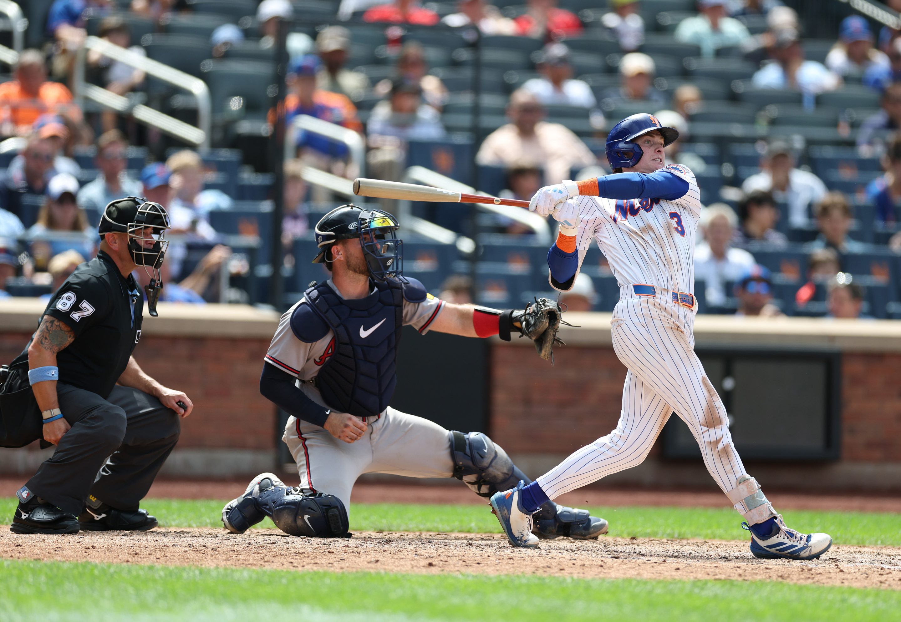 A baseball player swinging his bat with two umpires behind him.