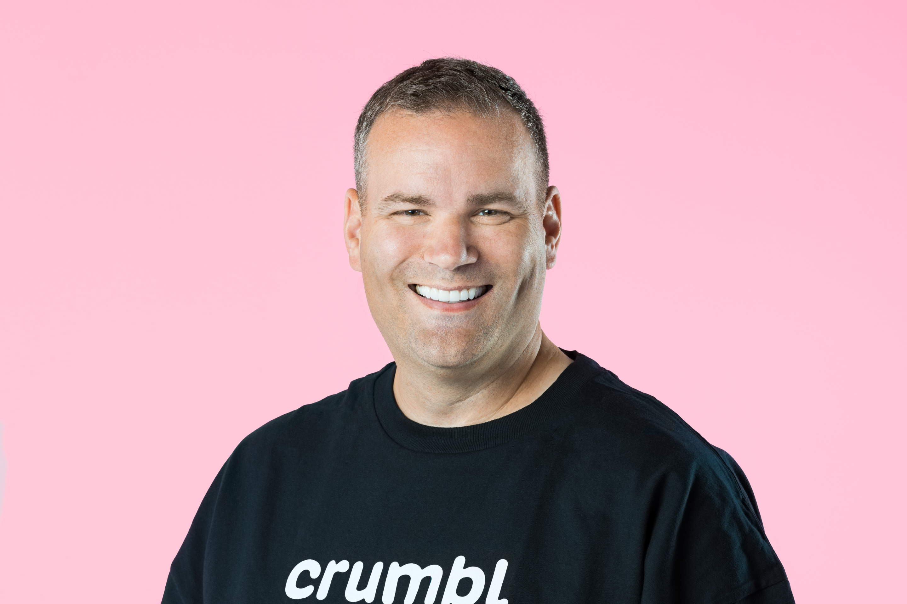 Jason McGowan headshot. Wearing a black shirt with 'Crumbl' behind a pink background