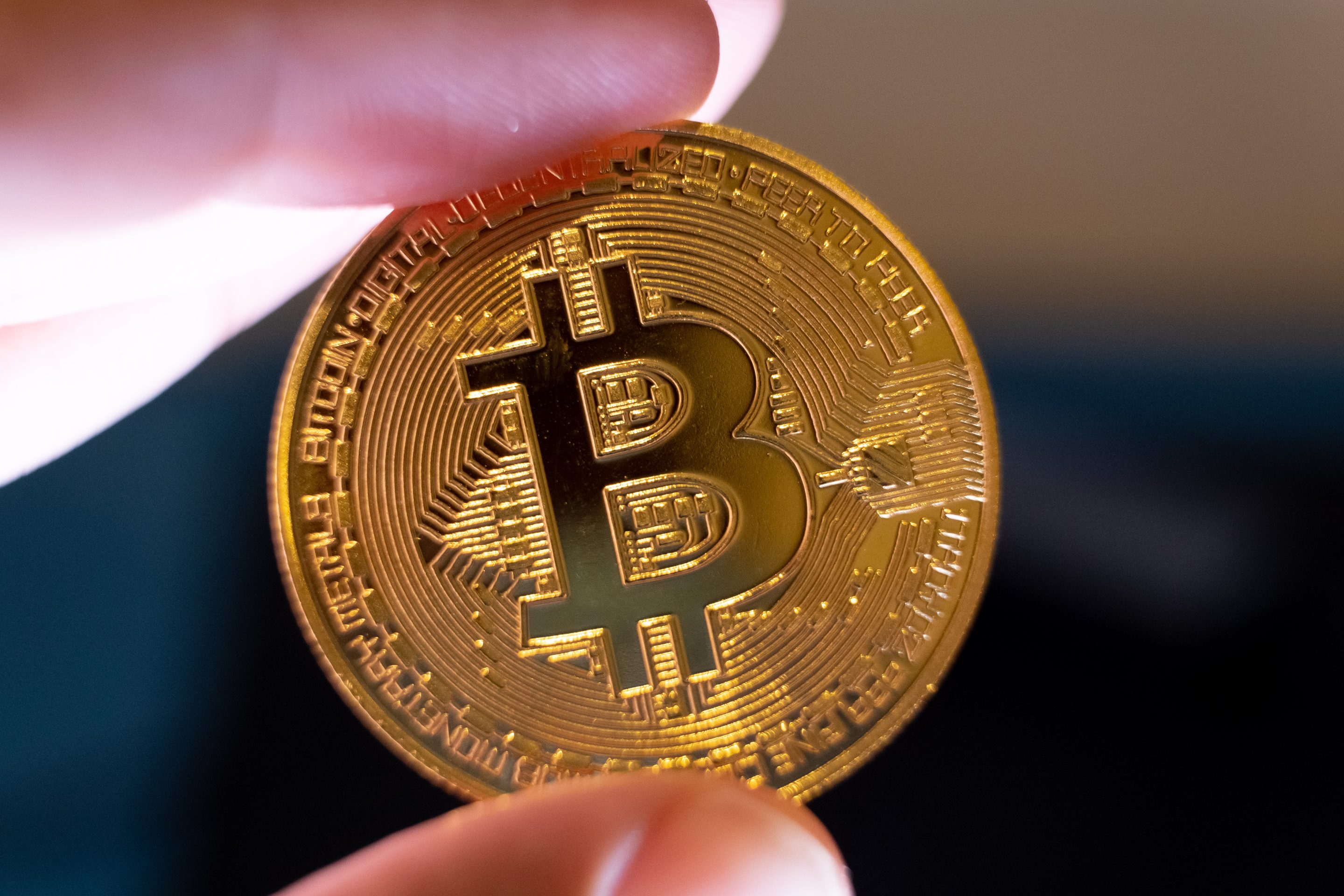 A physical Bitcoin coin held between an index finger and a thumb.