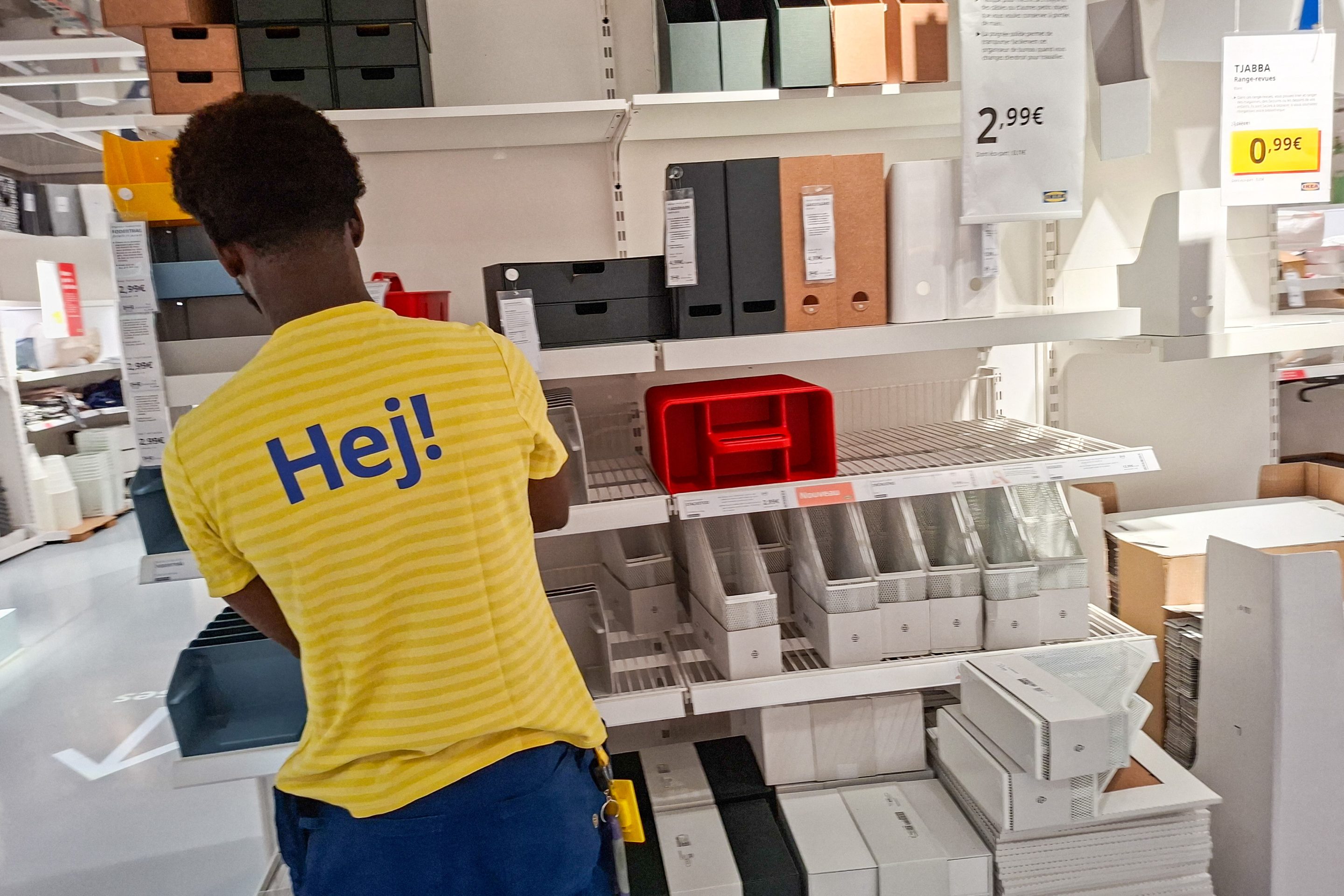 An employee wearing a yellow T-shirt with Hej printed on it stands in front of a storage aisle at the IKEA store in the Italie Deux shopping center in Paris, France, on July 27, 2026.