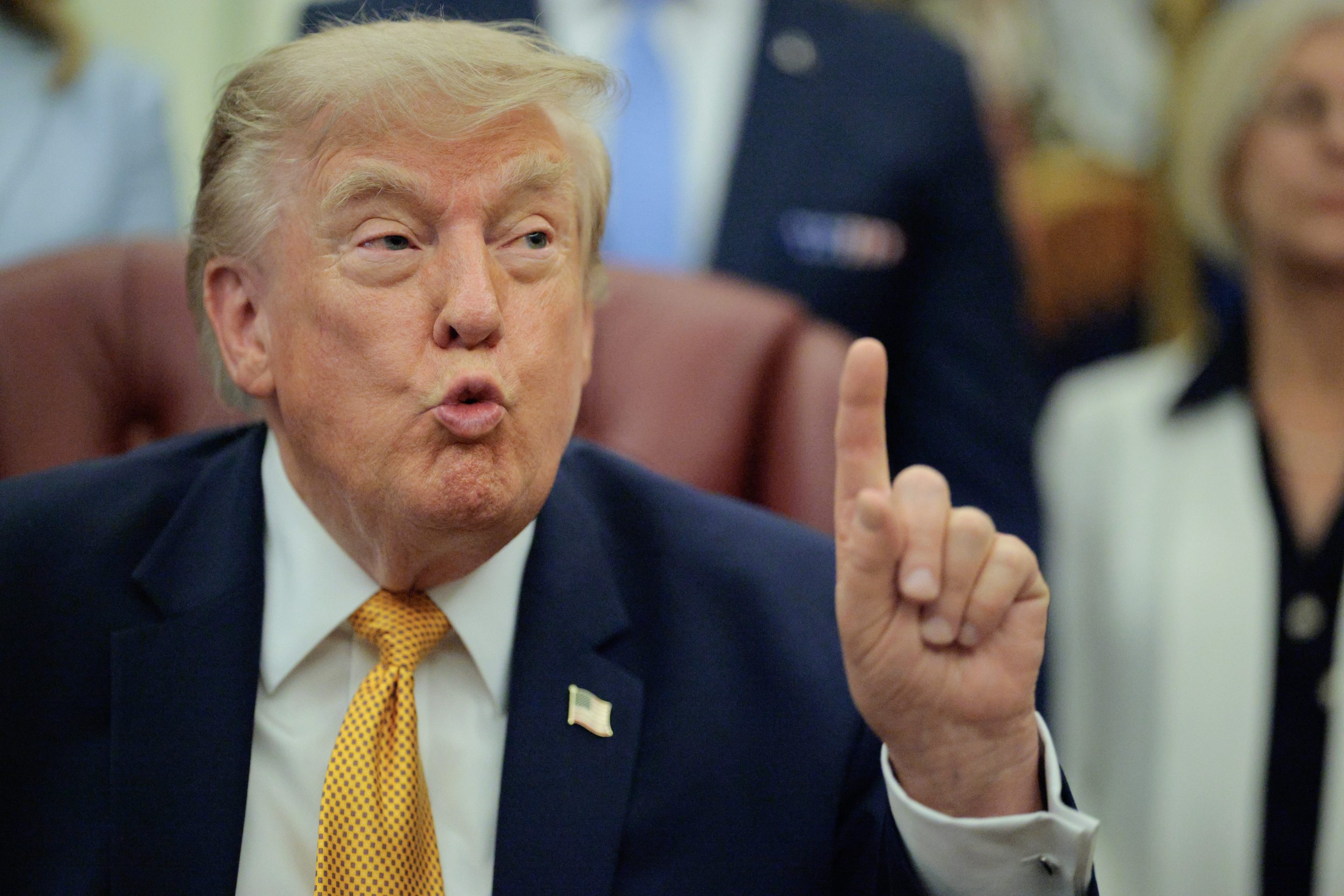 Donald Trump, in the middle of speaking, holds up his hand with his pointer finger extended.